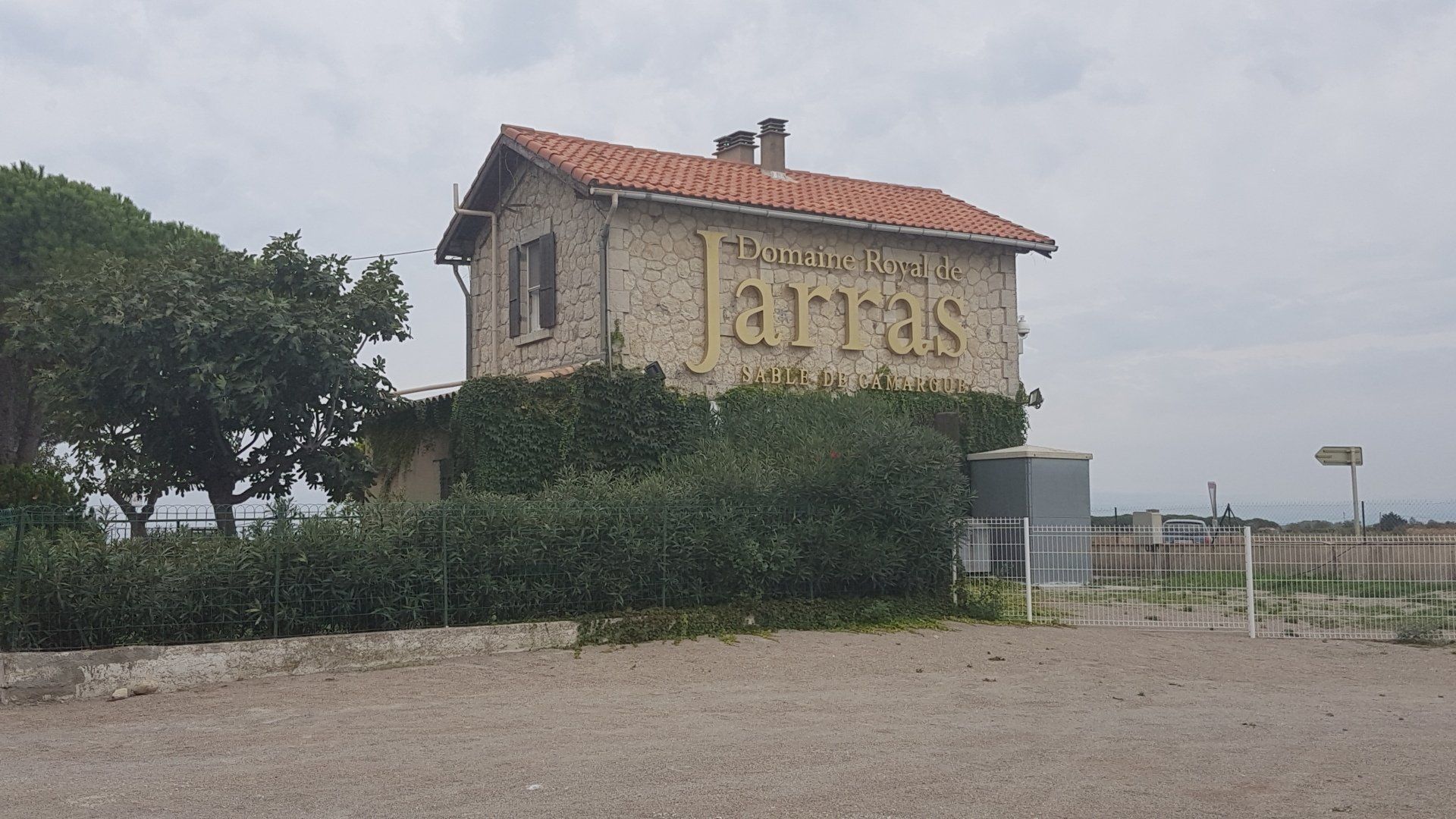 Gebäude aus Stein mit rotem Dach - Oleander davor und Werbung des Weingutes am Haus Jarras