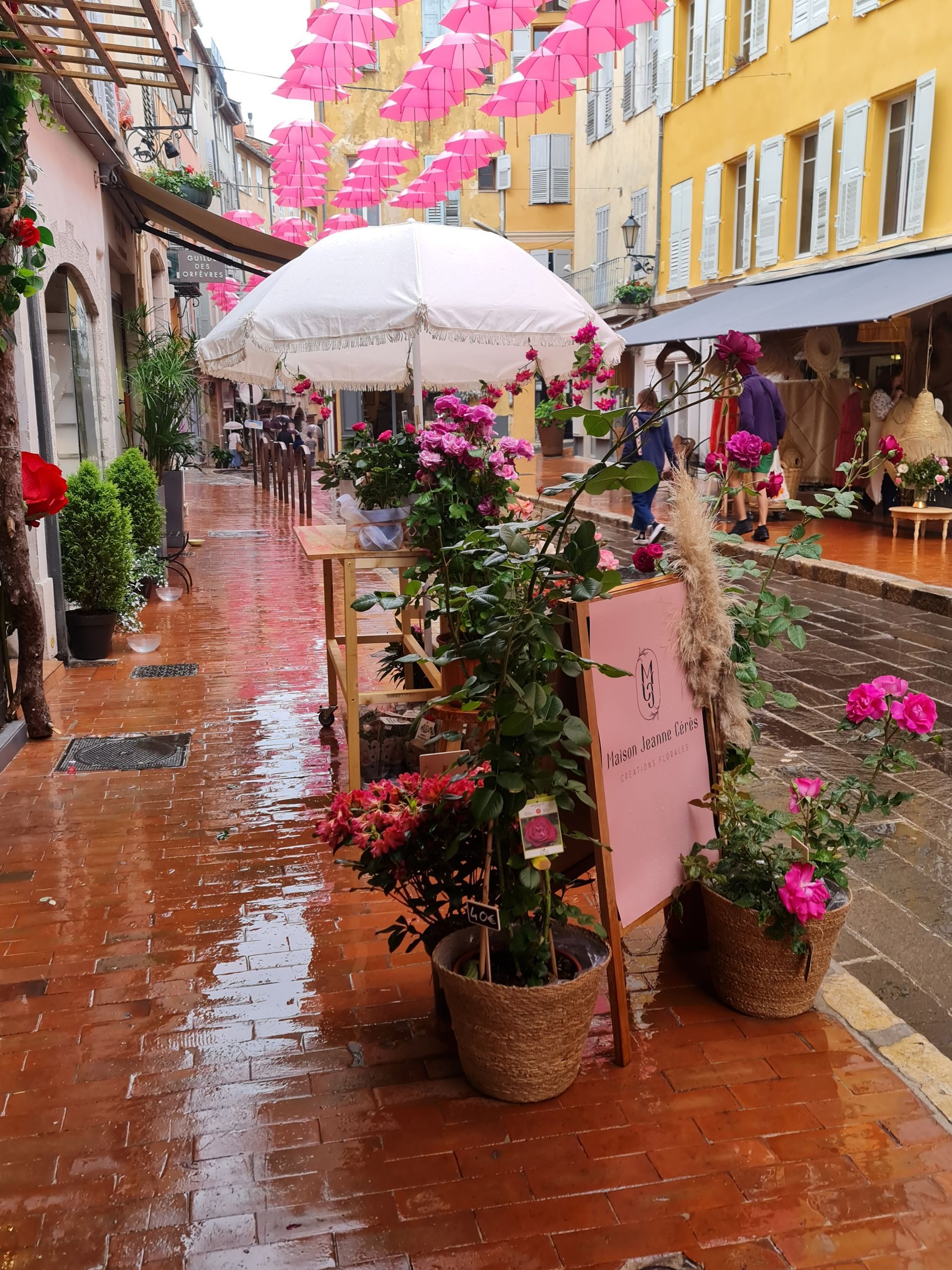 kleine Gasse mit rosa Schirmen oben auf der Straße steht ein weißer Schirm mit rosa Rosen