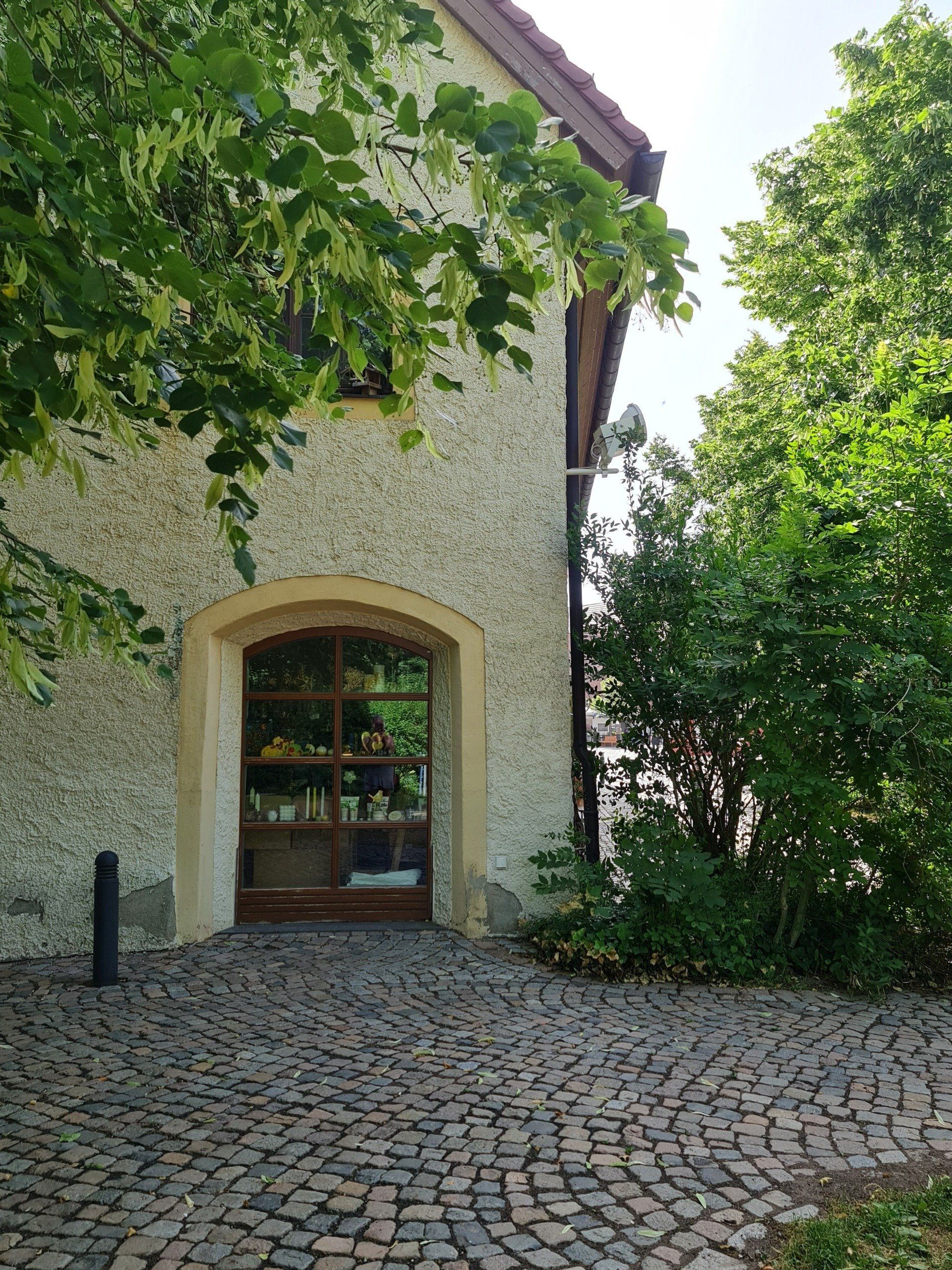 Blick auf ein Haus mit braunem Ladenfenster unten Bäume davor