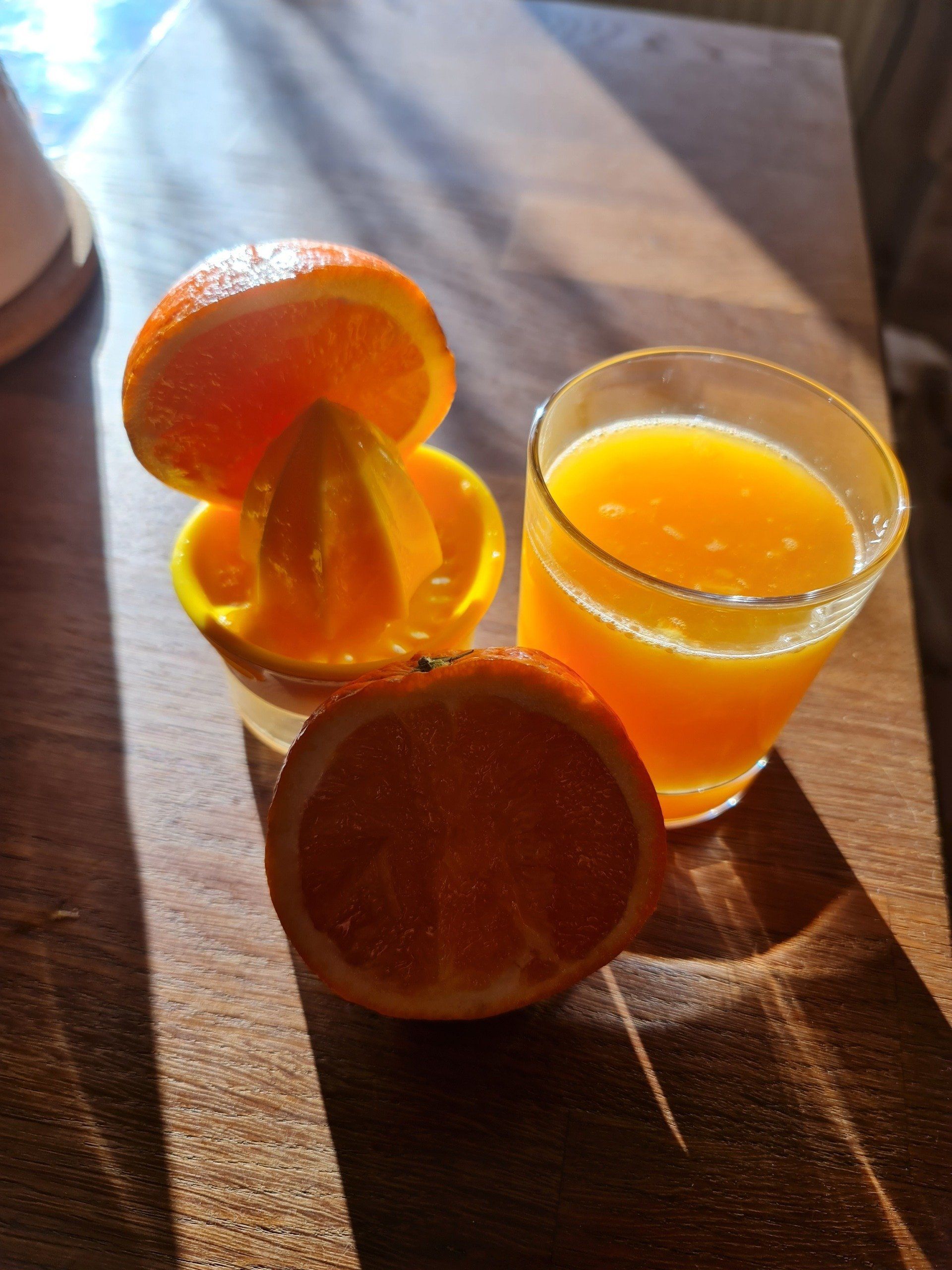 Orangensaft im Glas und 2 halbe Orangen und Zitruspresser