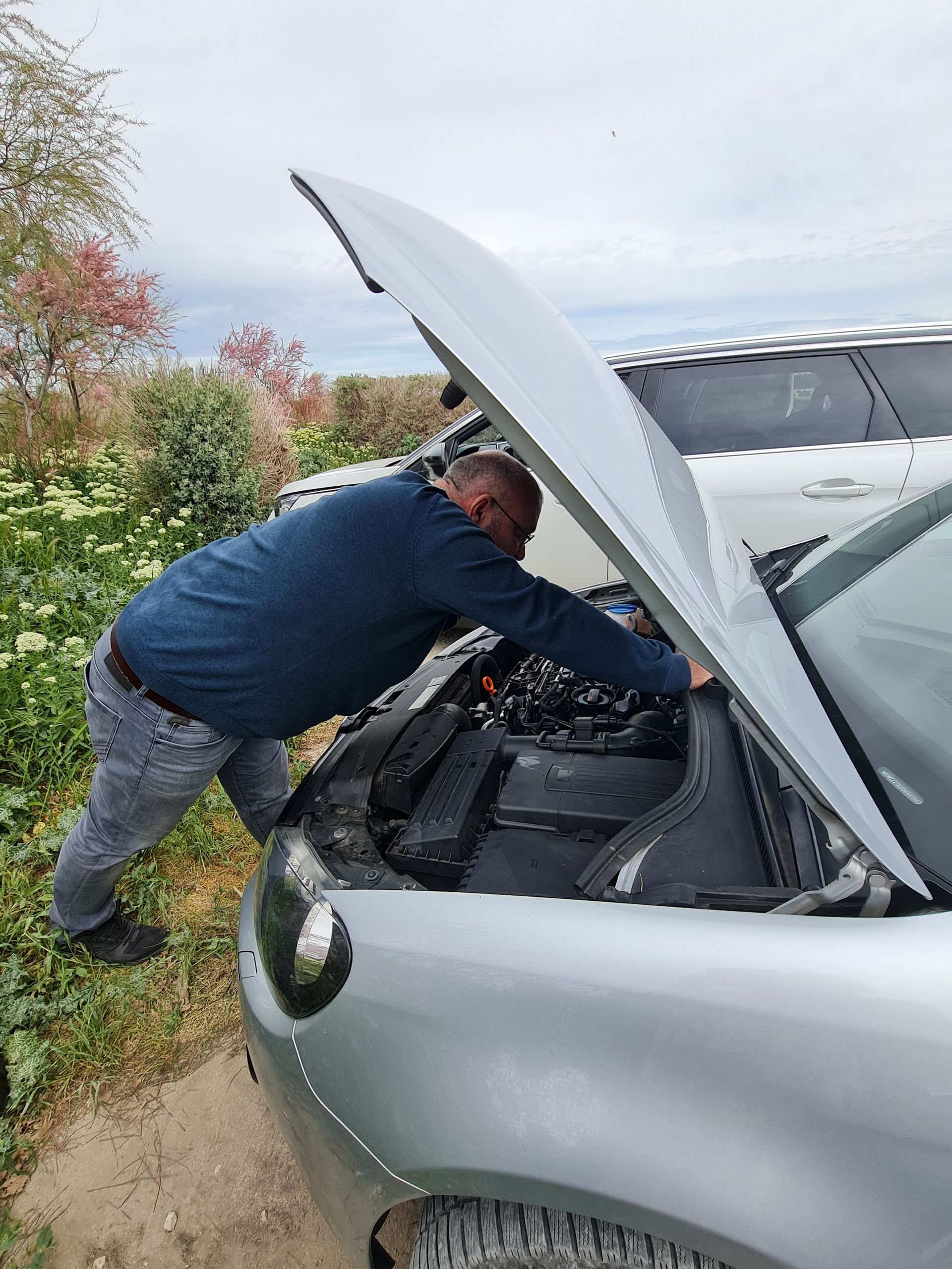 Mann schaut in den Motorraum eines silbernen Autos