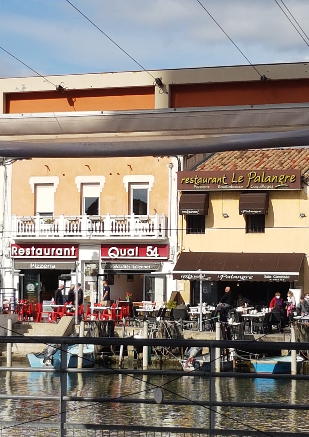 orange Häuser mit Restaurants, rot beschriftet und Tische mit Stühlen am Wasser auf der anderen Seite des Kanals Le Grau du Roi