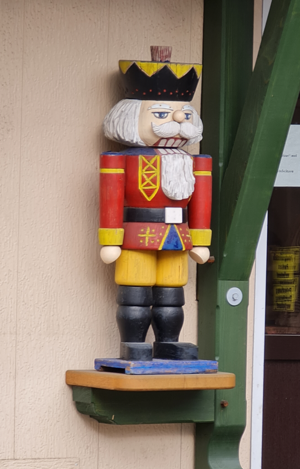 Nußknacker 50 cm groß steht auf einer Empore rote Jacke gelbe Hose und Stiefel in schwarz Bart und Haare weiß schwarzer Hut