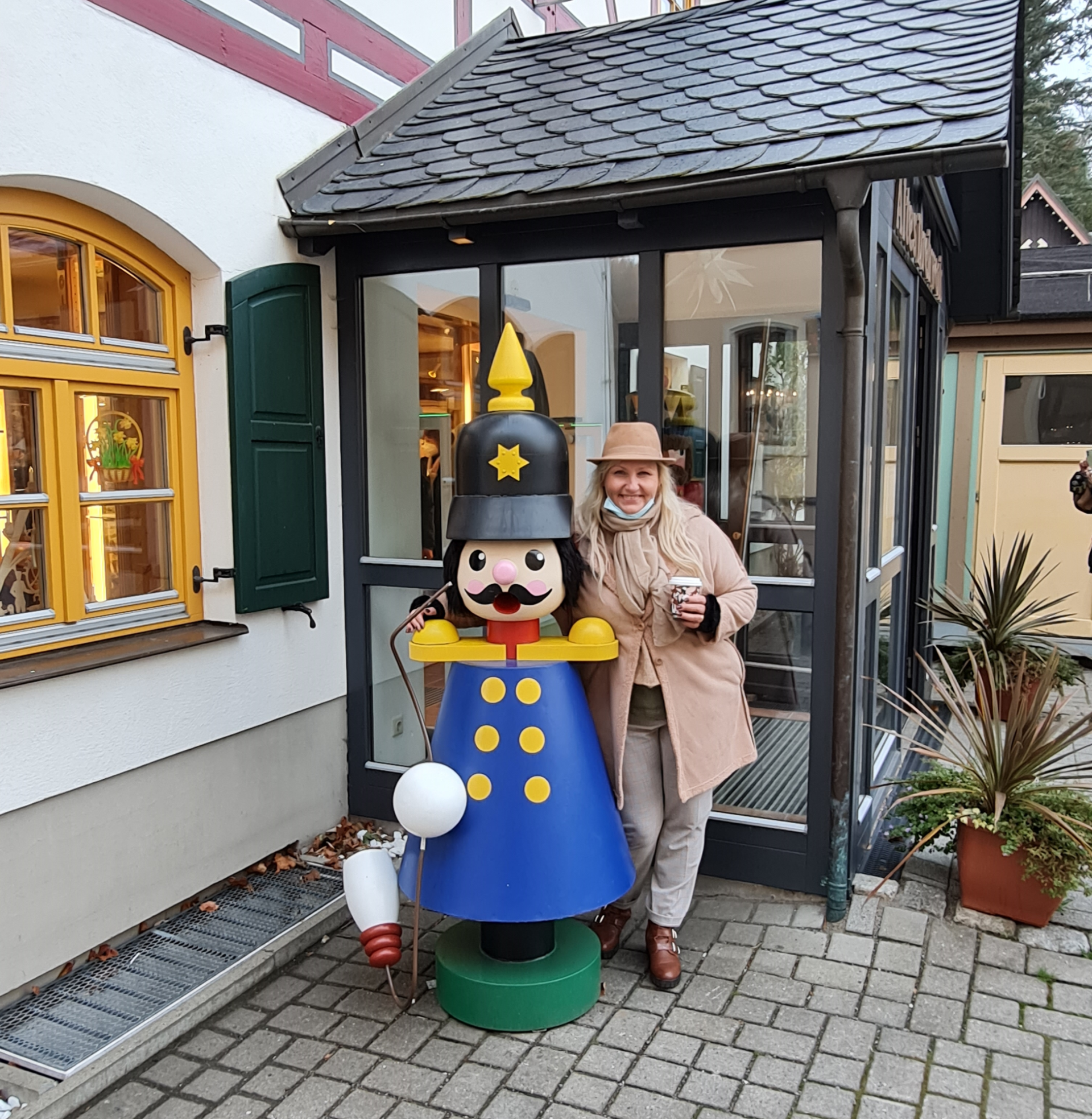 Liebe Grüße bis zum nächsten Besuch - es war ein toller Tag hier in Seiffen-Erzgebirge Fachwerkhaus mit großem blauen Räuchermann davor und einer Frau daneben sie umarmt den Räuchermann es ist Herbst keine Sonne
