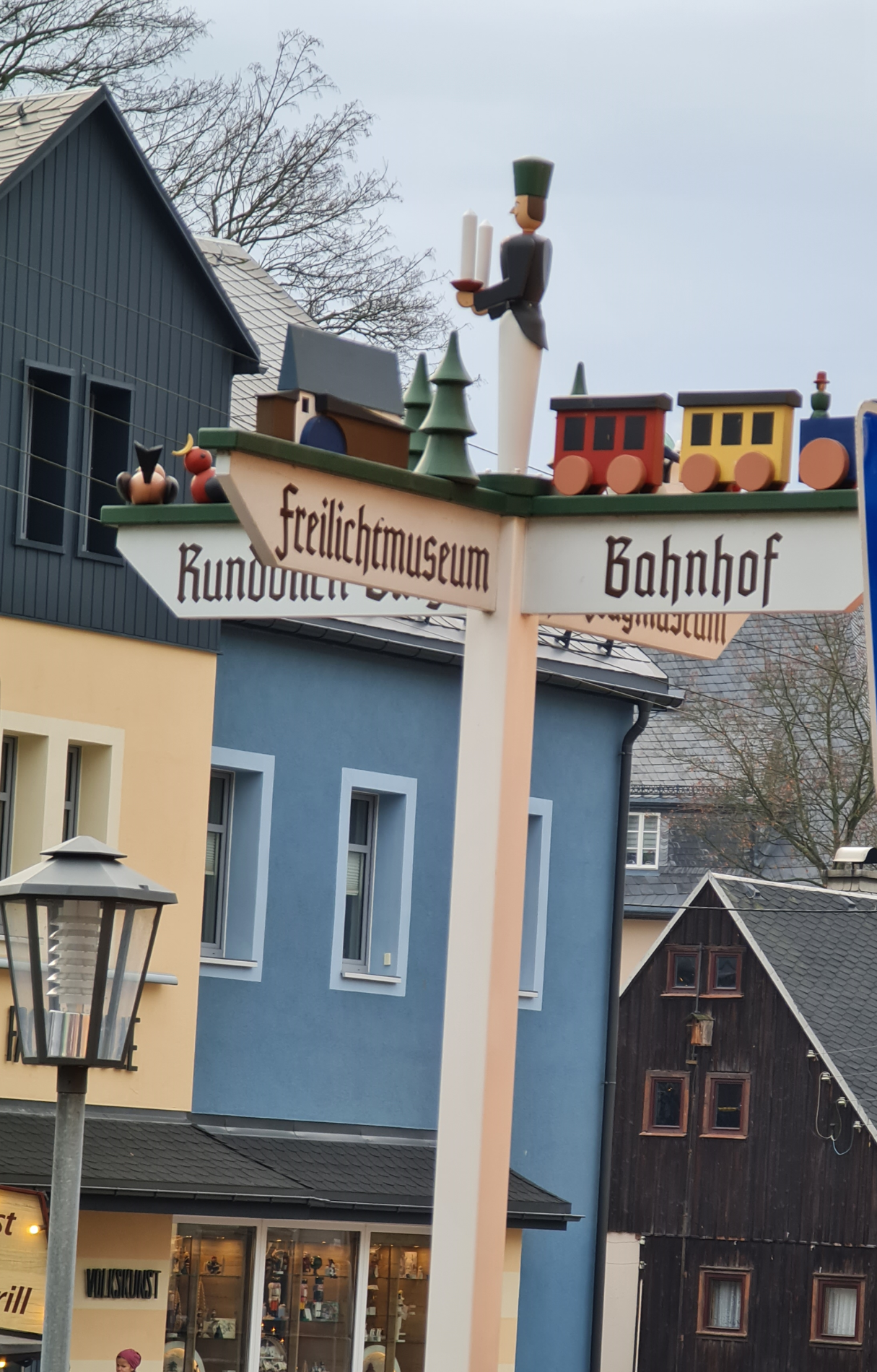 Die Richtung weisen mit Spielsachen aus Holz - eine süße Ideen Hinweisschild mit bunten Holzfiguren und kleiner Eisenbahn obenaufim Ort Seiffen in verschiedene Richtungen Bahnhof Freilichtmuseum
