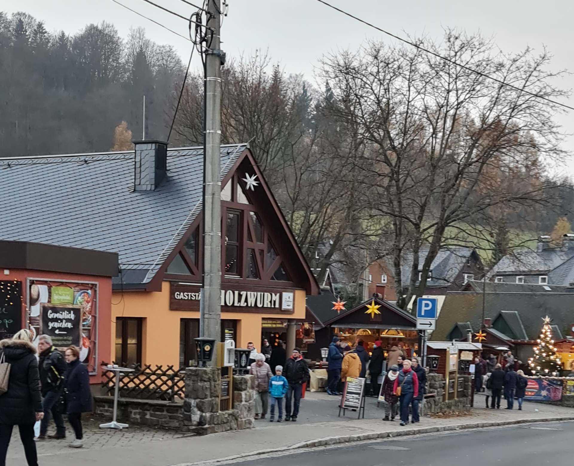 kleiner Weihnachtsmarkt an der Straßae in Seiffen, leuchtende Sterne sind aufgehängt Menschen schauen und laufen da entlang