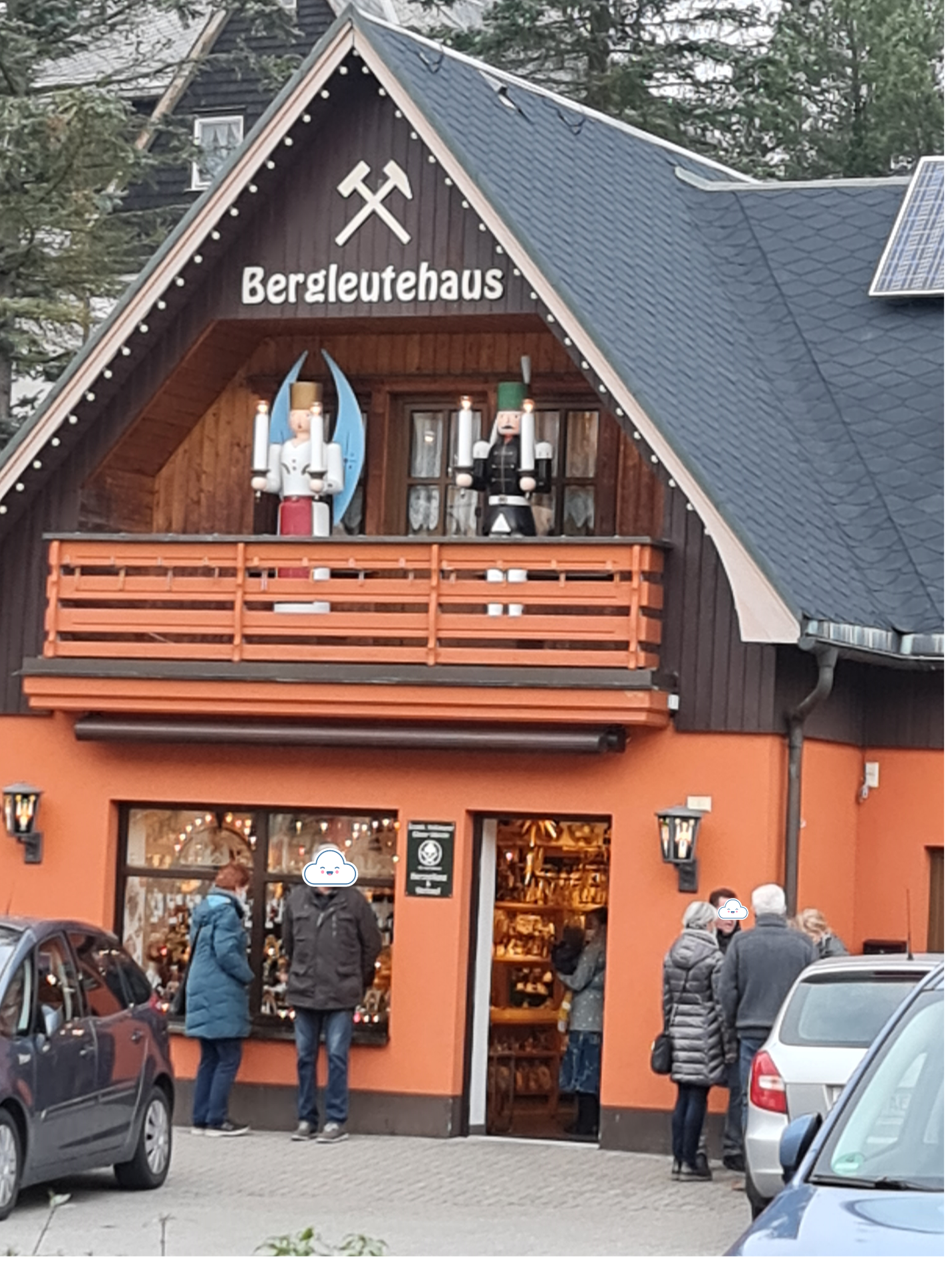 oranges Haus mit Balkon darauf eine großer weißer Engel und ein schwarzer Bergmann aus Holz gedrechselt und bemalt