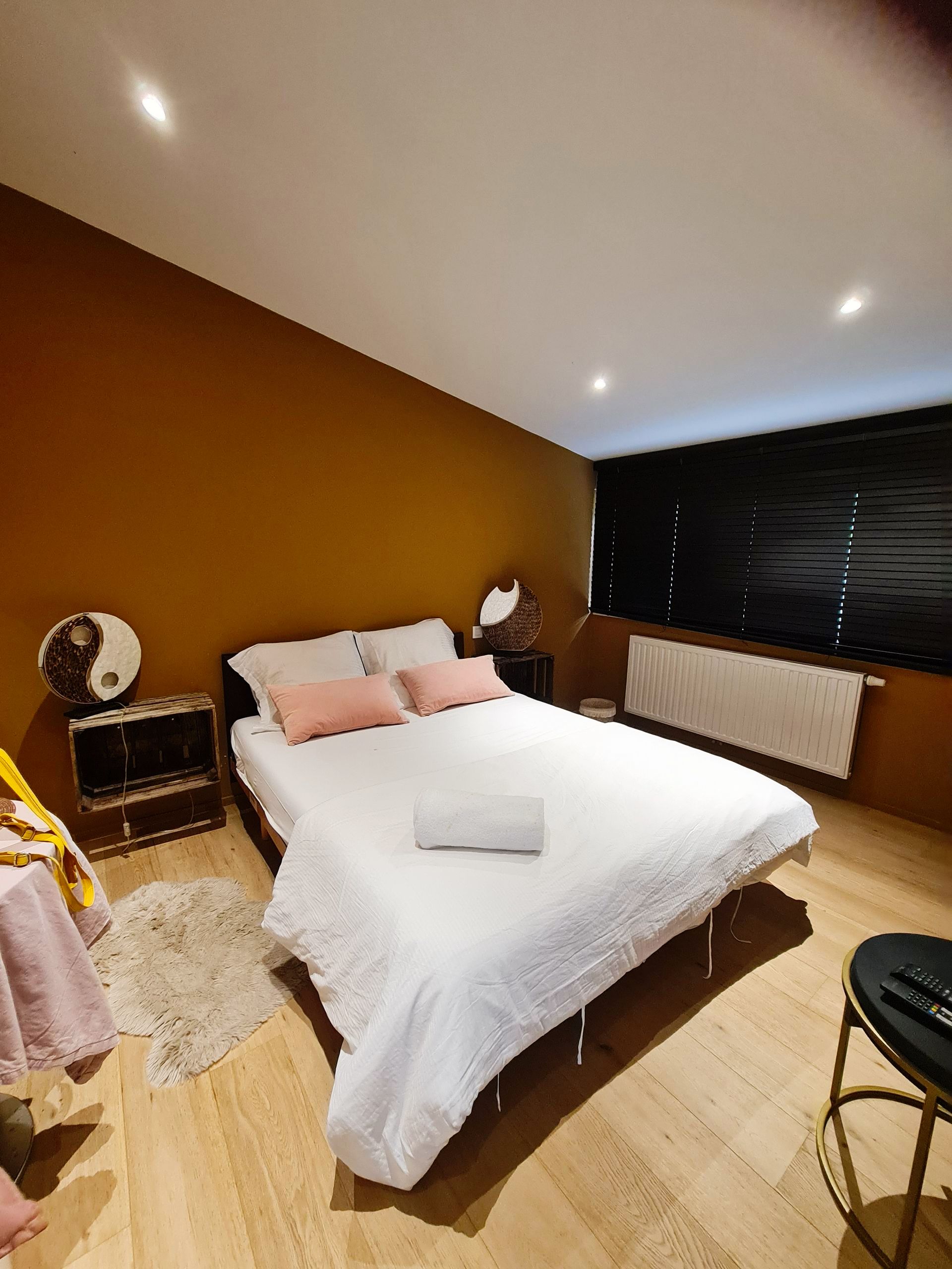 Zimmer mit braunen Wänden, weiss bezogenes Doppelbett und rosa Kissen