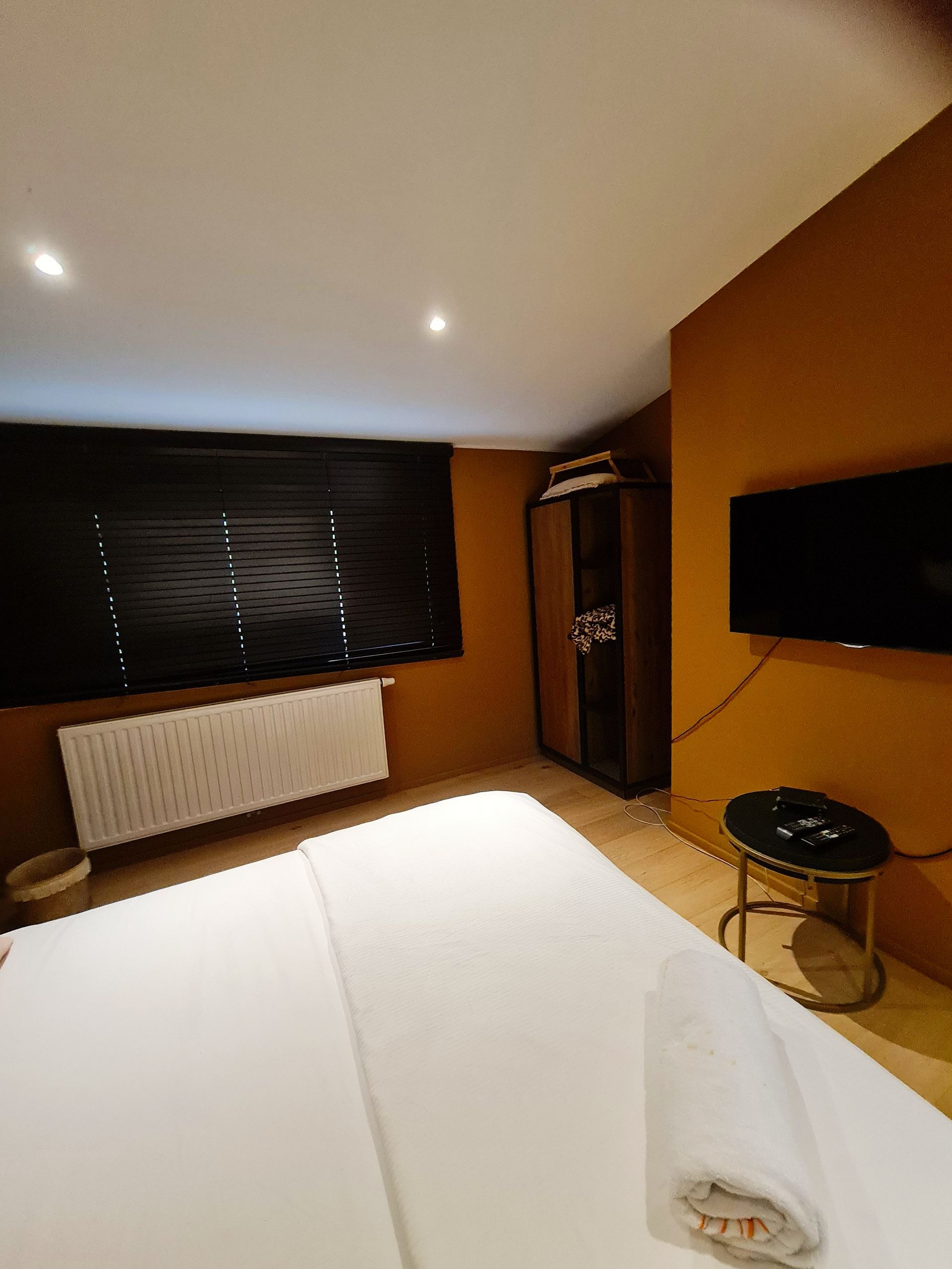 Zimmer mit großem Fenster mit brauner Jalousie und weiss bezogenes Doppelbett und rosa Kissen