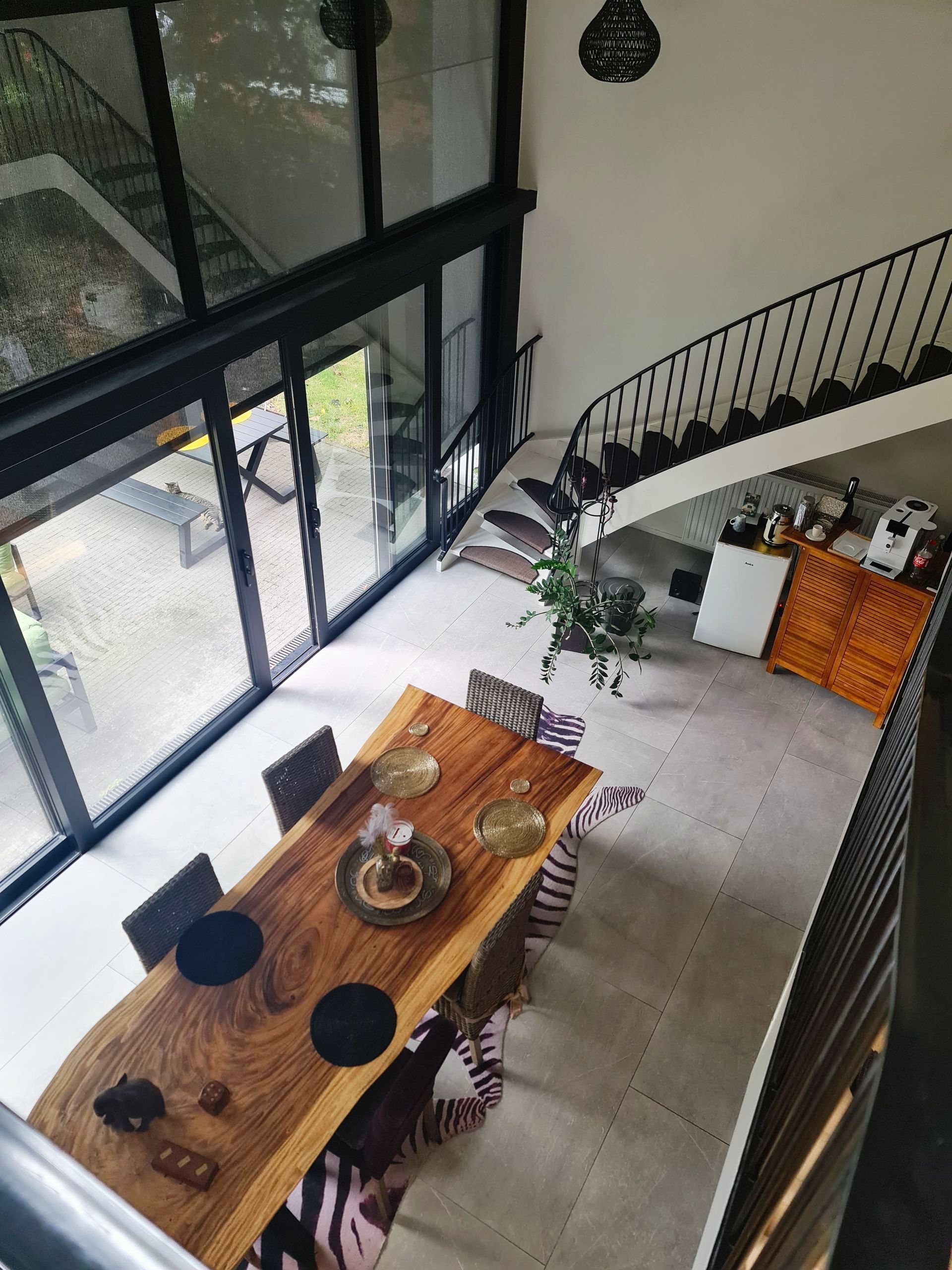 Blick vom Geländer der Galerie in den unteren Raum mit großem Tisch und eine große Glasfront zum Garten.