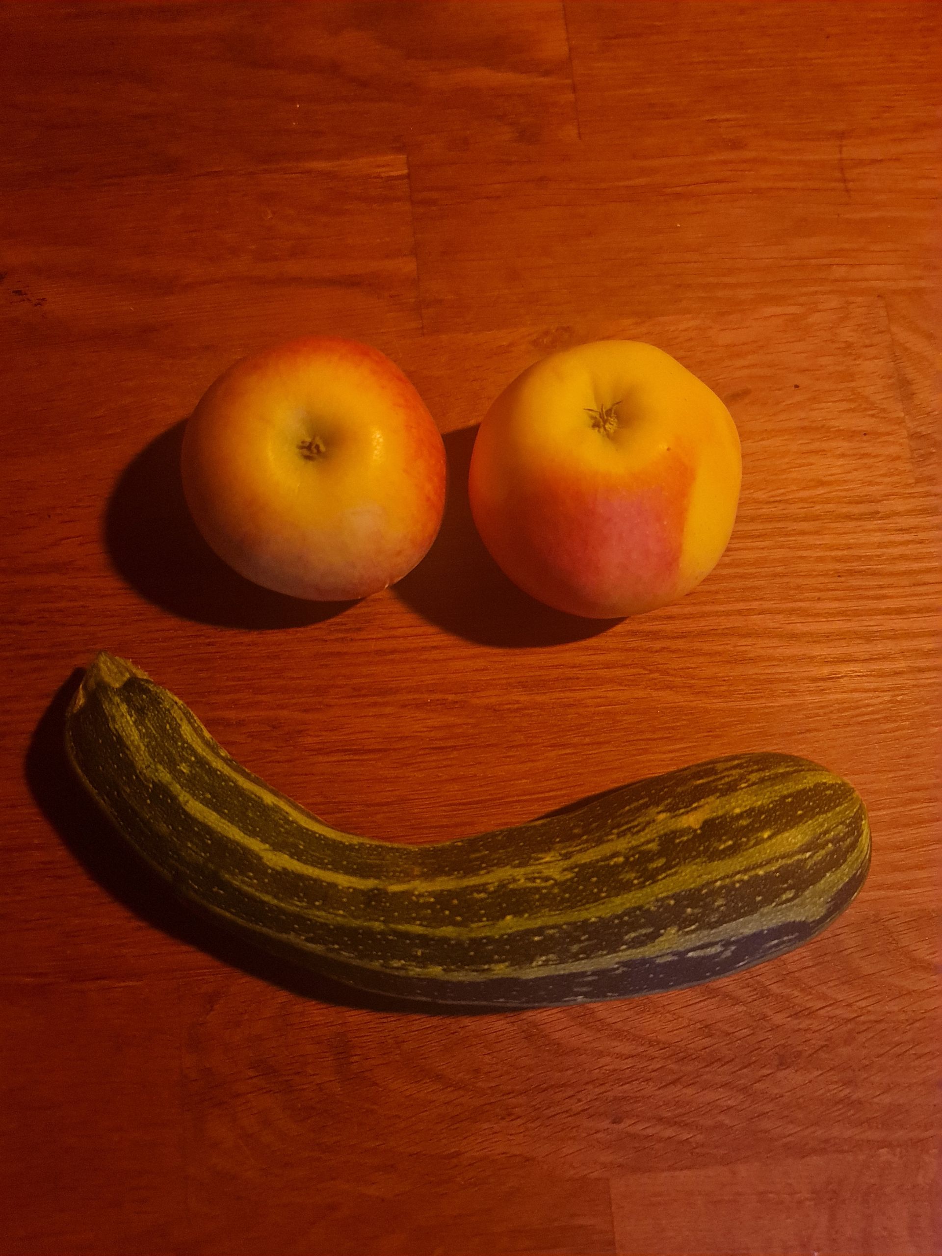 Zucchini als lächelnder Mund und 2 Äpfel als Augen