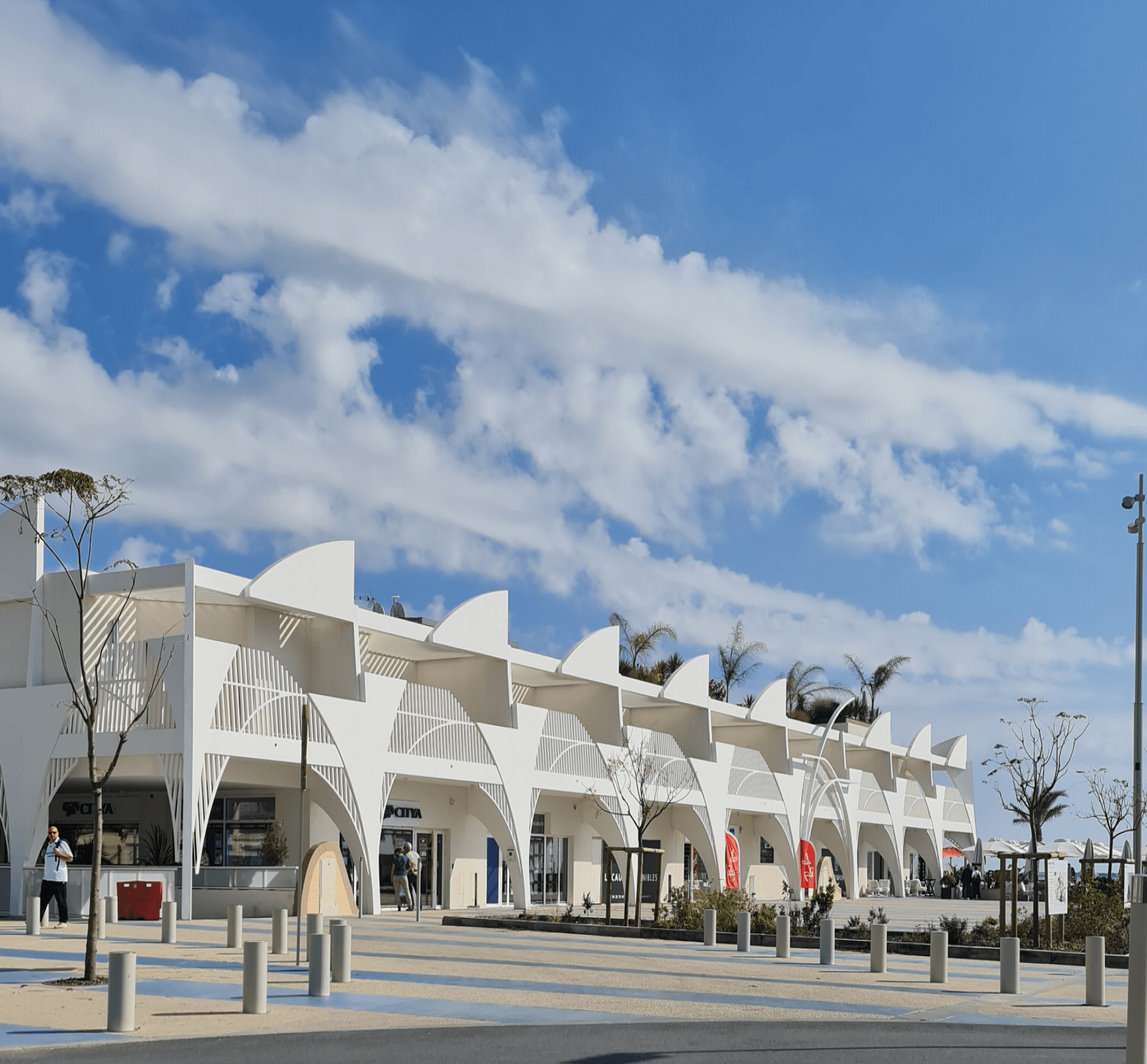 weißes flaches Gebäude mit unterbrochener Struktur blauer Himmel mit einzelnen weißen Wolken