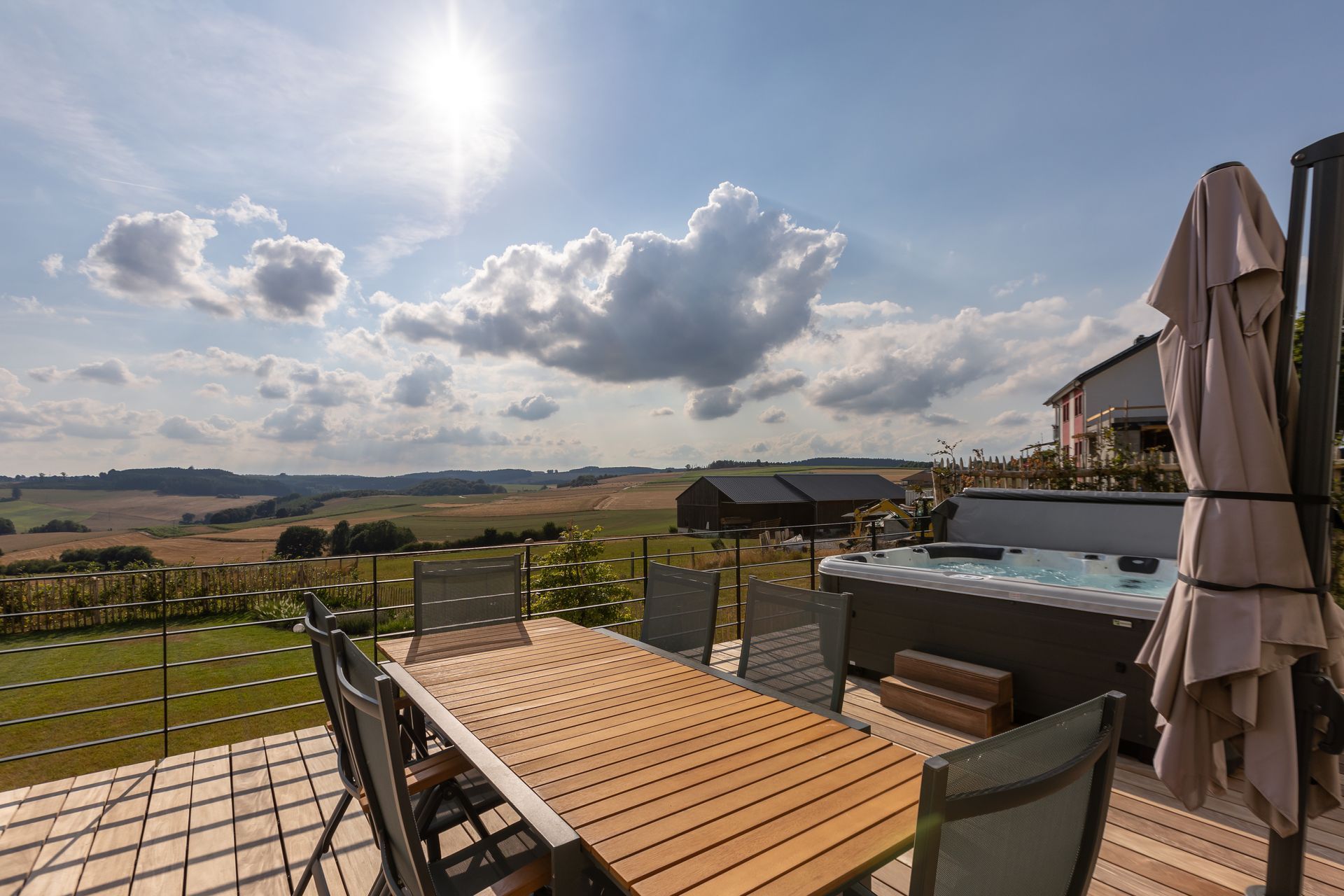 Aussicht von der Terrasse Terrasse des Resort of Spirit mit Whirlpool und großem Esstisch mit sechs Stühlen – umgeben von grünen Feldern und Wäldern mit weitem Ausblick in die Natur.
