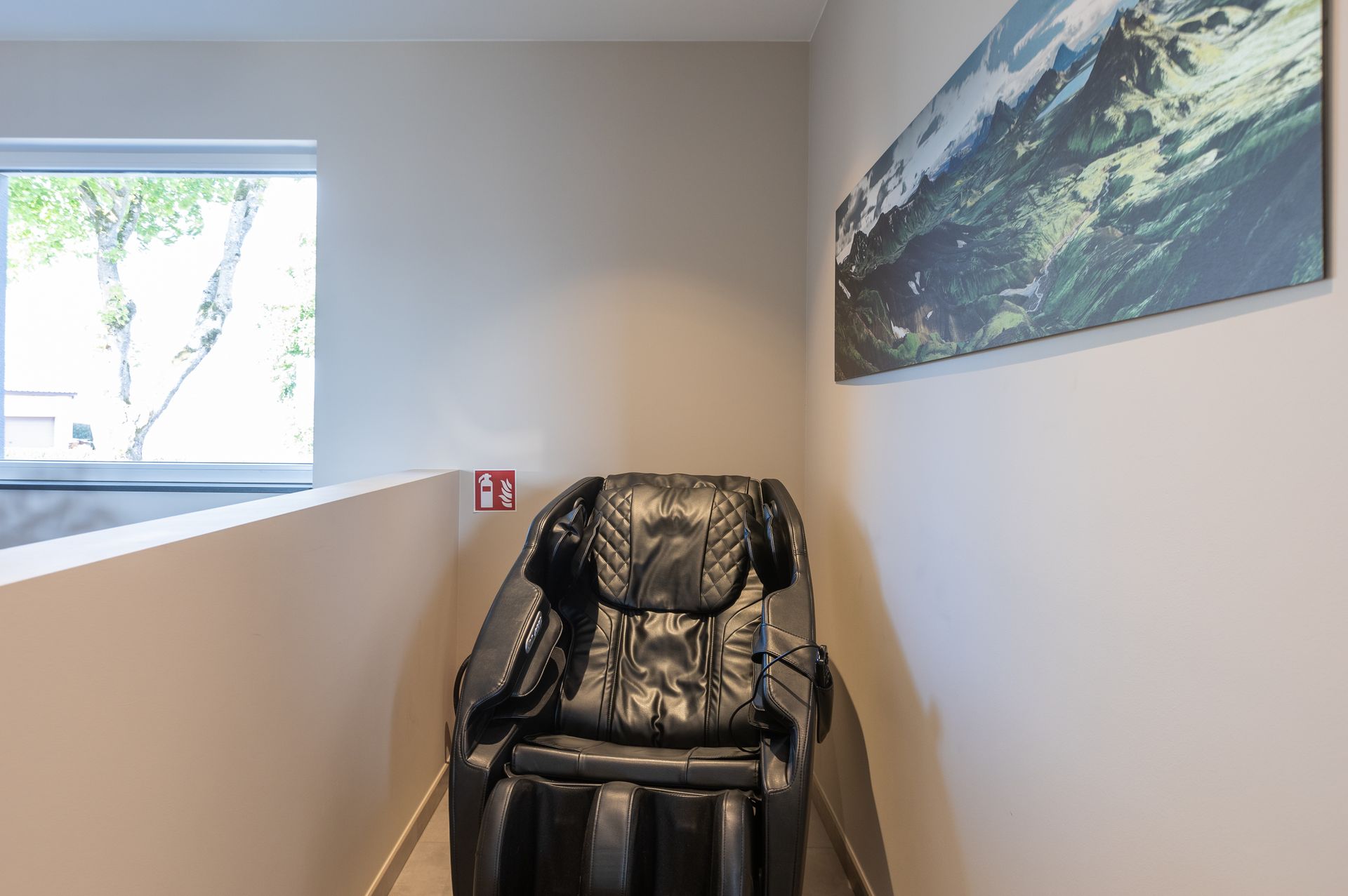 In einer Nische steht ein dunkelbrauner, Lederbezogener Massagesessel. Rechts an der Wand hängt ein gläsernes Naturbild mit grünen WIesen.