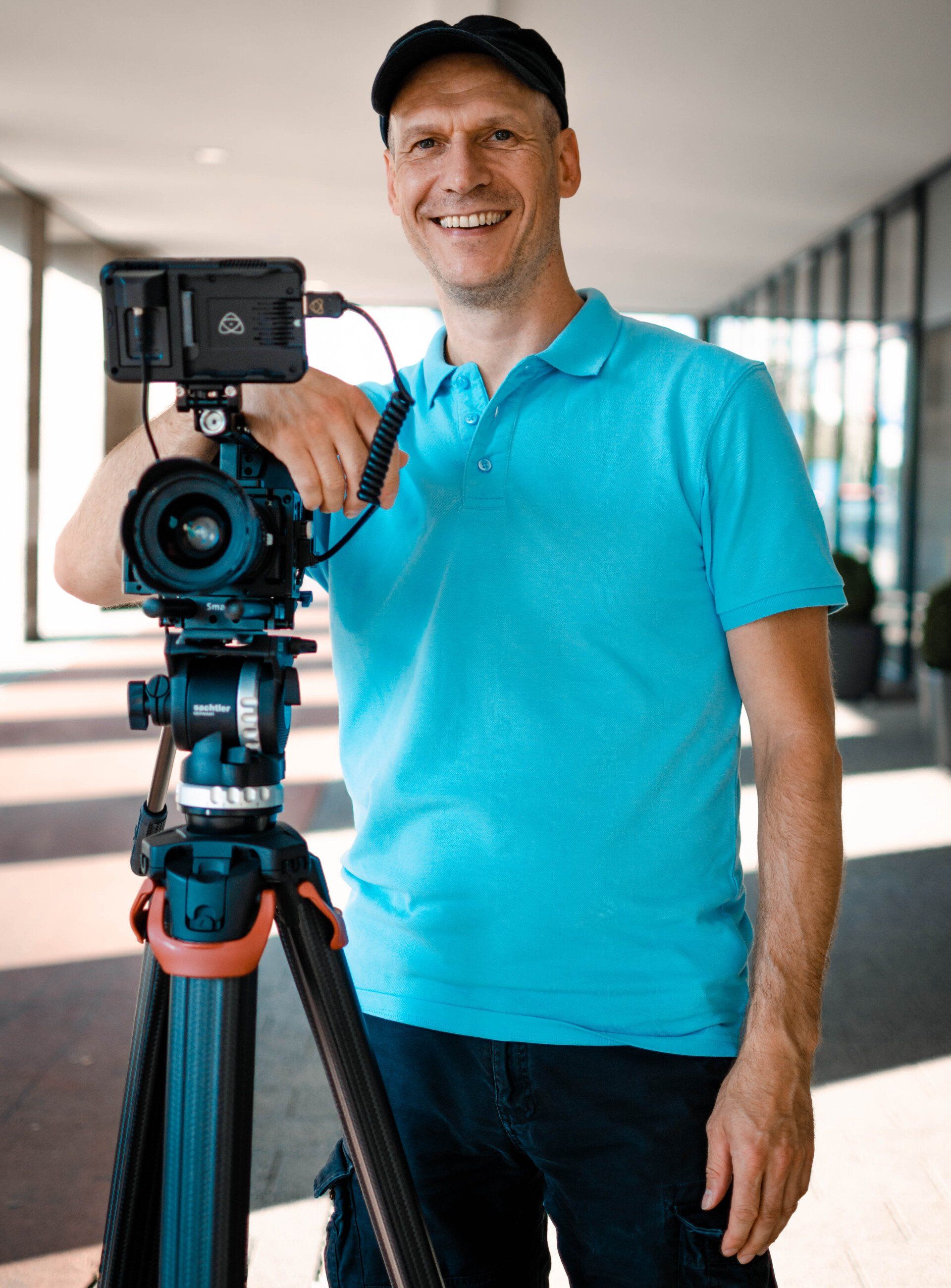 Mann mit Filmkamera lächelt in die Kamera – professionelles Businessportrait bei Outdoorshooting in Leipzig