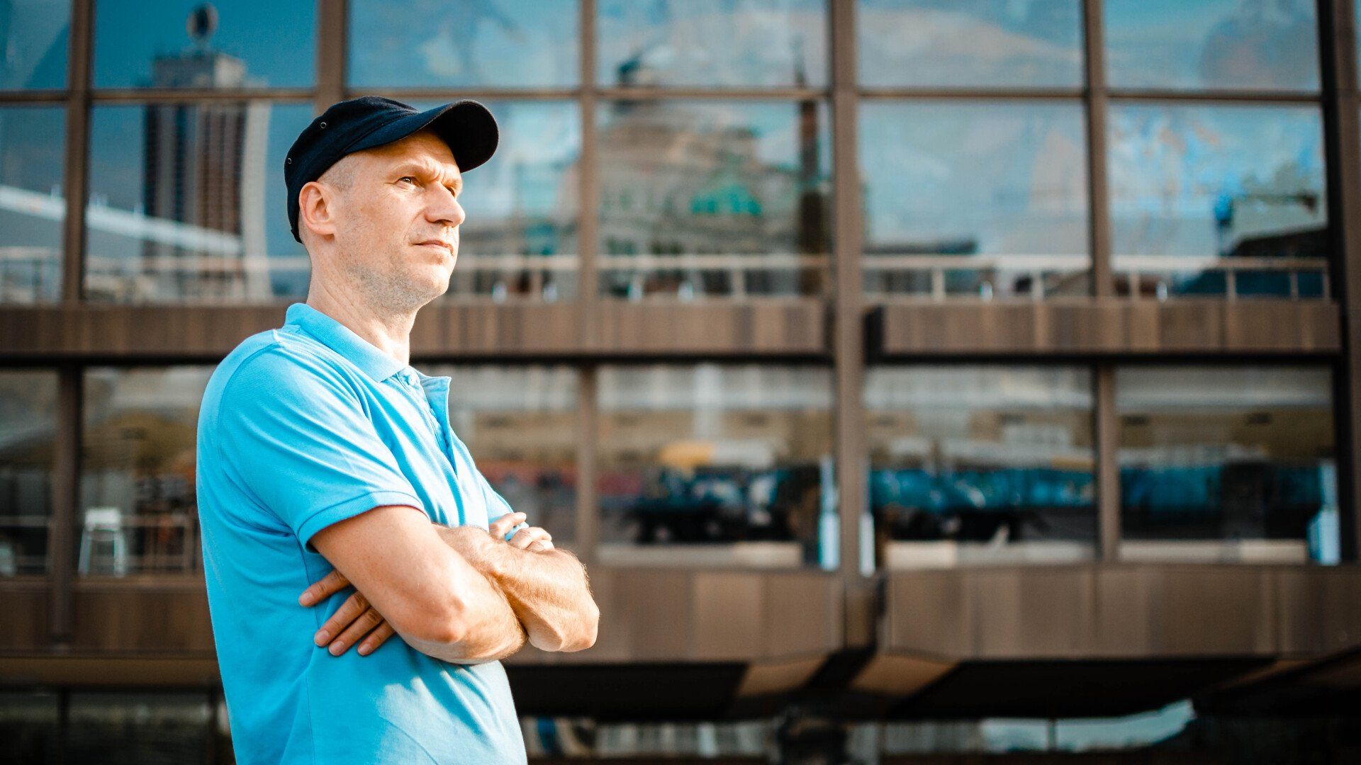 Mann mit verschränkten Armen im blauen Polohemd vor Glasfassade – modernes Outdoor-Businessportrait in Leipzig