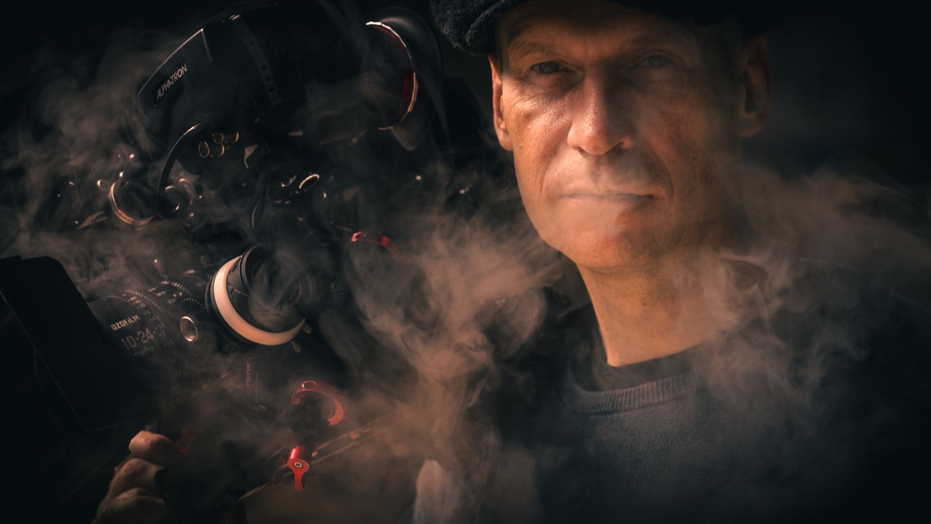 Ausdrucksstarkes Portrait eines Mannes mit Kamera, umgeben von Rauch in dunkler Atmosphäre