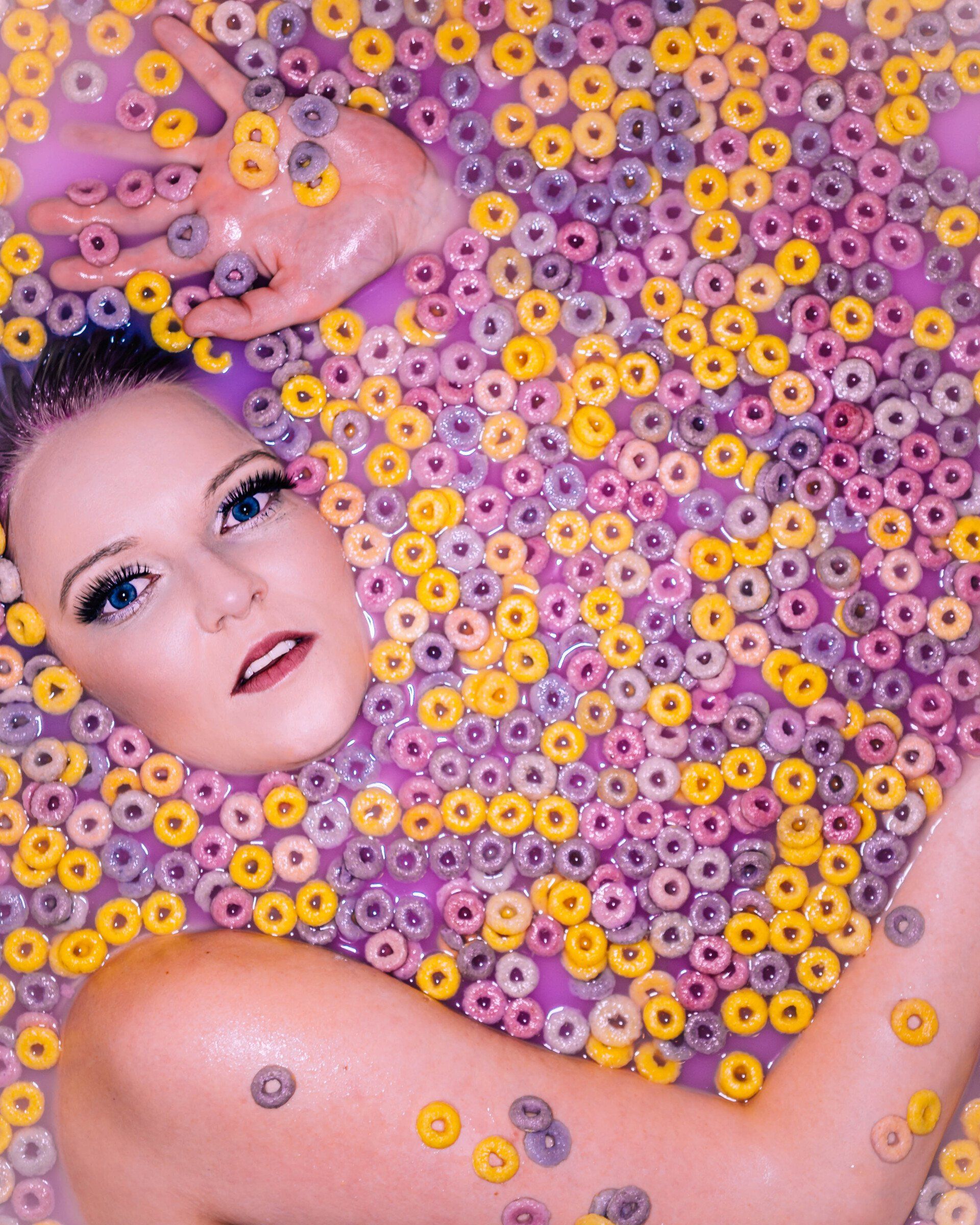 Frau liegt in violetter Milch mit bunten Cereals – kreatives, surreal-poppiges Portraitfoto aus einem Milkbath-Shooting in Leipzig