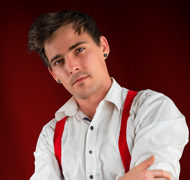 Portrait von Kevin Wesenberg – Hochzeitsfotograf aus Leipzig mit weißen Hemd, roten Hosenträgern und tätowiertem Unterarm vor rotem Hintergrund