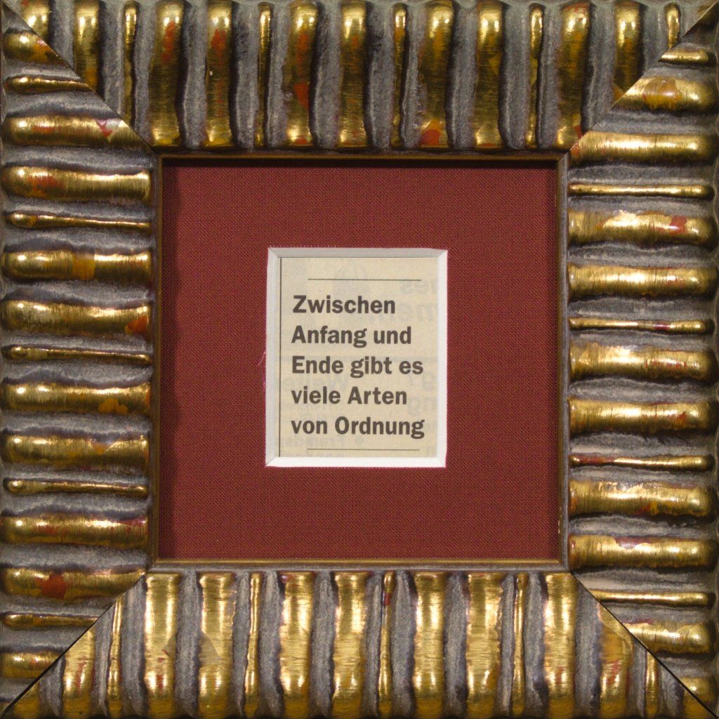 Gerahmter Zeitungssatz im Goldrahmen: „Zwischen Anfang und Ende gibt es viele Arten von Ordnung“.