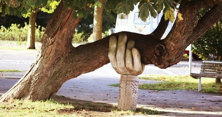 Wooden sculpture of a hand supporting a falling tree