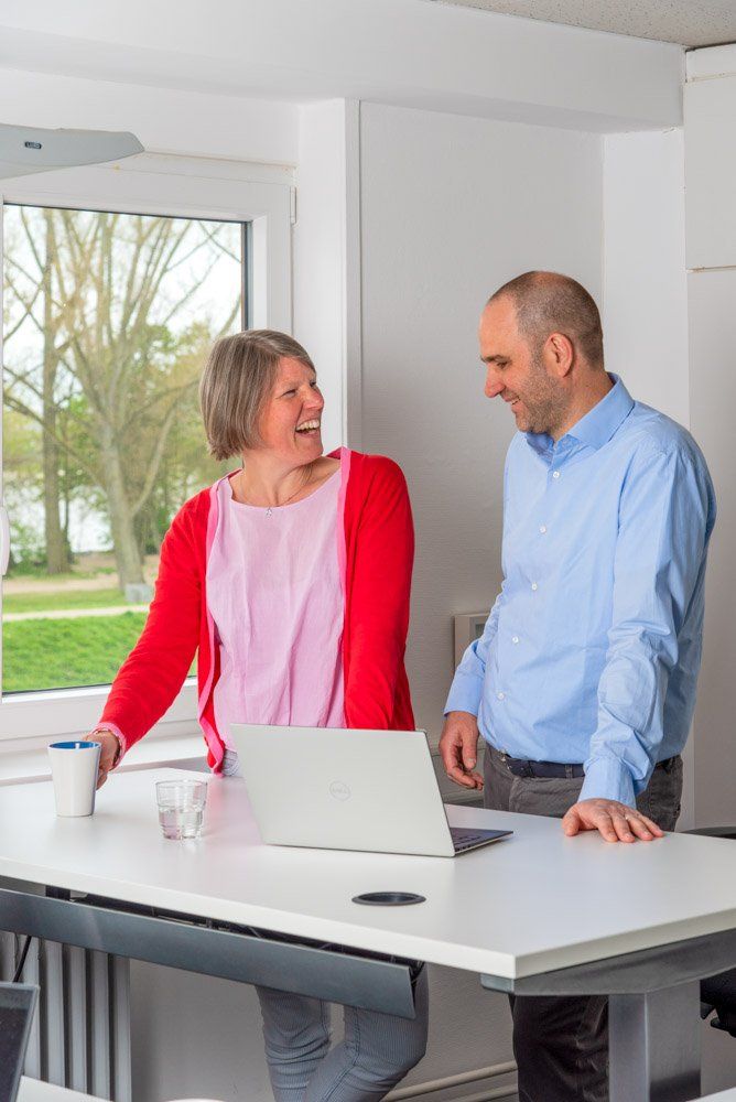 Ehepaar steht lachend hinter einem Schreibtisch