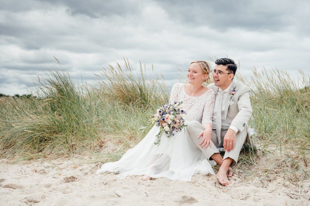 Brautpaar sitzt am Strand und schaut in die Ferne