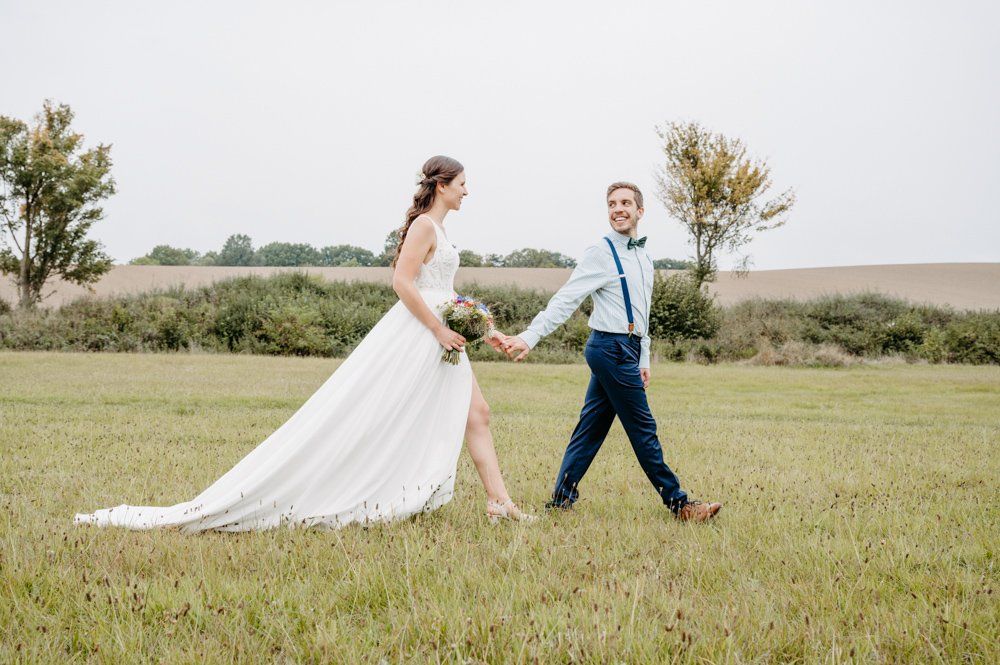 Brautpaar geht mit schnellen Schritten über eine Wiese