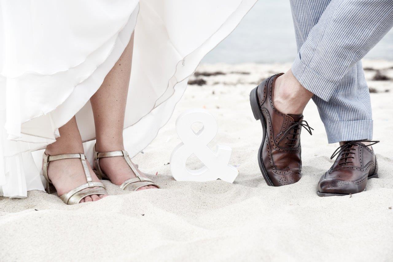 <img src=”Hochzeitsfotograf-Kiel-Füße-eines-Brautpaares-mit-&-Zeichen.jpg” alt=”Füße eines Brautpaares am Strand mit & Zeichen dazwischen”>