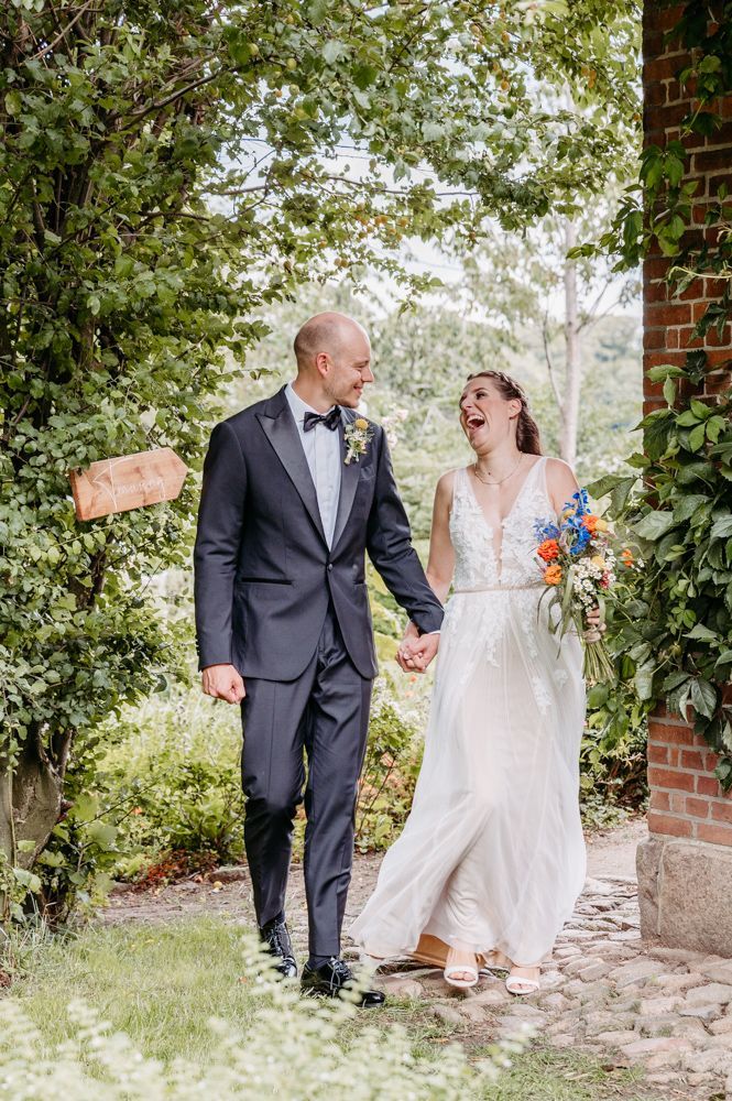 Brautpaar geht lachend zur Trauung in der Hofscheune Bissee