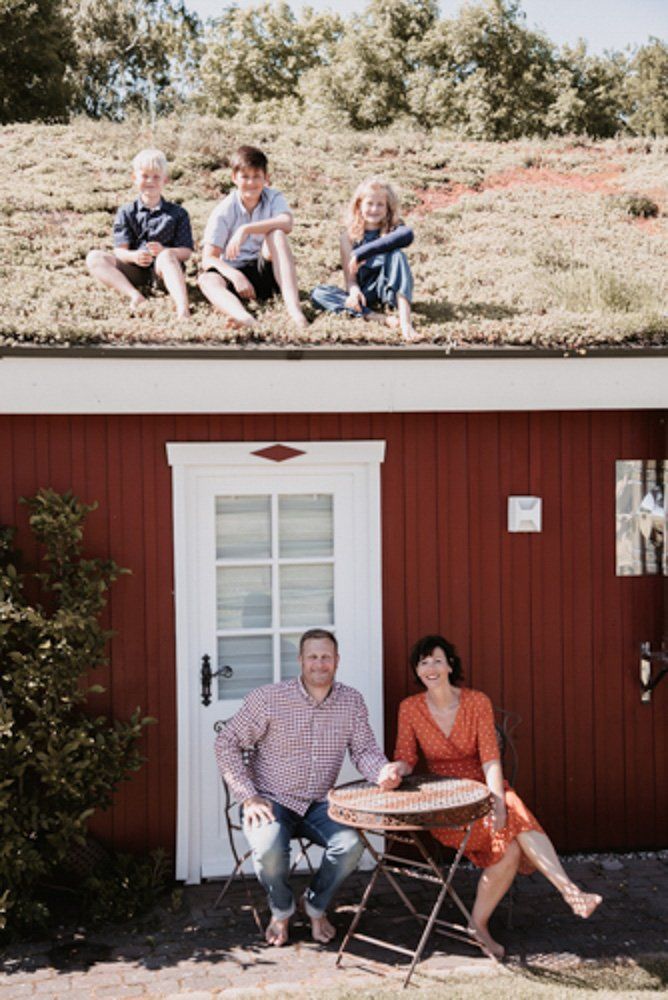 Familienfoto, Eltern sitzen vor dem ferienhaus auf der Bank, die Kinder sitzen auf dem Dach