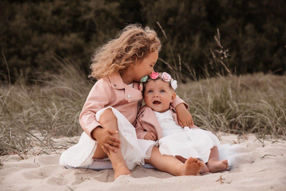 2 Geschwister am Starnd, große Schwester gibt kleiner Schwester einen Kuss
