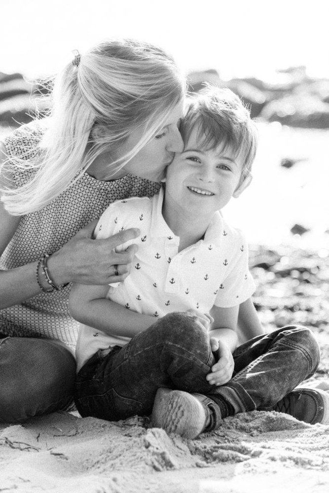 Mutter und Sohn sitzend am Strand, Mutter gibt Sohn einen Kuss auf die Wange