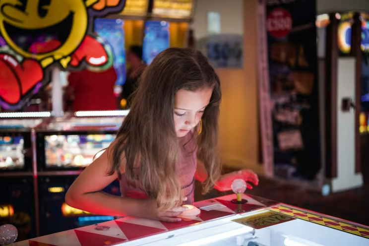 an image of a young girl playing on an arcade machine at haven cala gran there is an image of pac man in the background