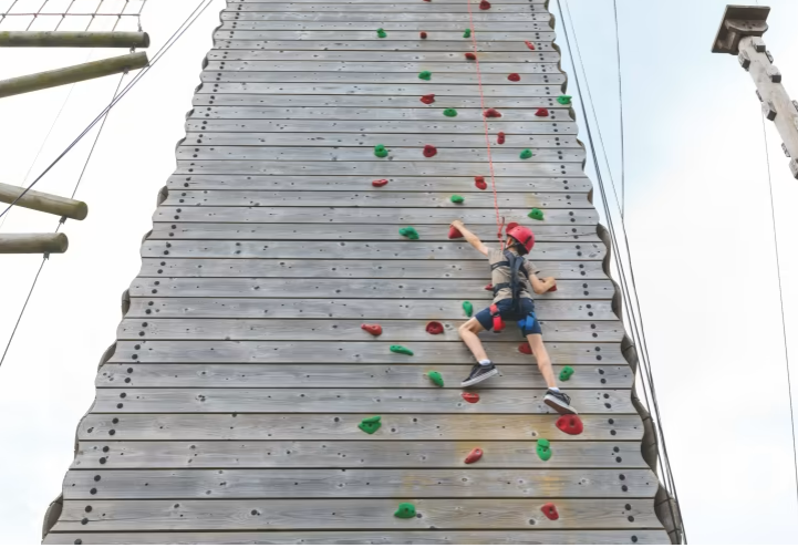 an image of the wooden climbing wall showing a girl climbing up the front of the wall in a helmet and a harness