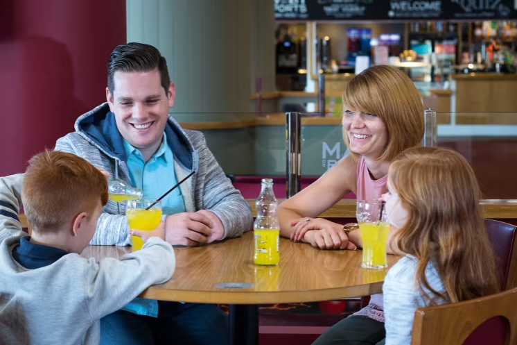 an image of a family sat at the table all drinking orange juice
