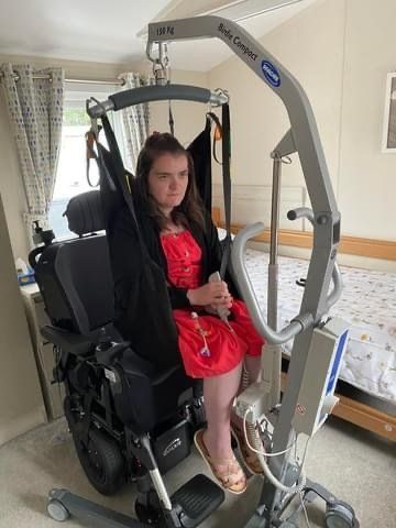 an image of a young lady using the electric mobile hoist as she transfers from her wheelchair to the profiling bed