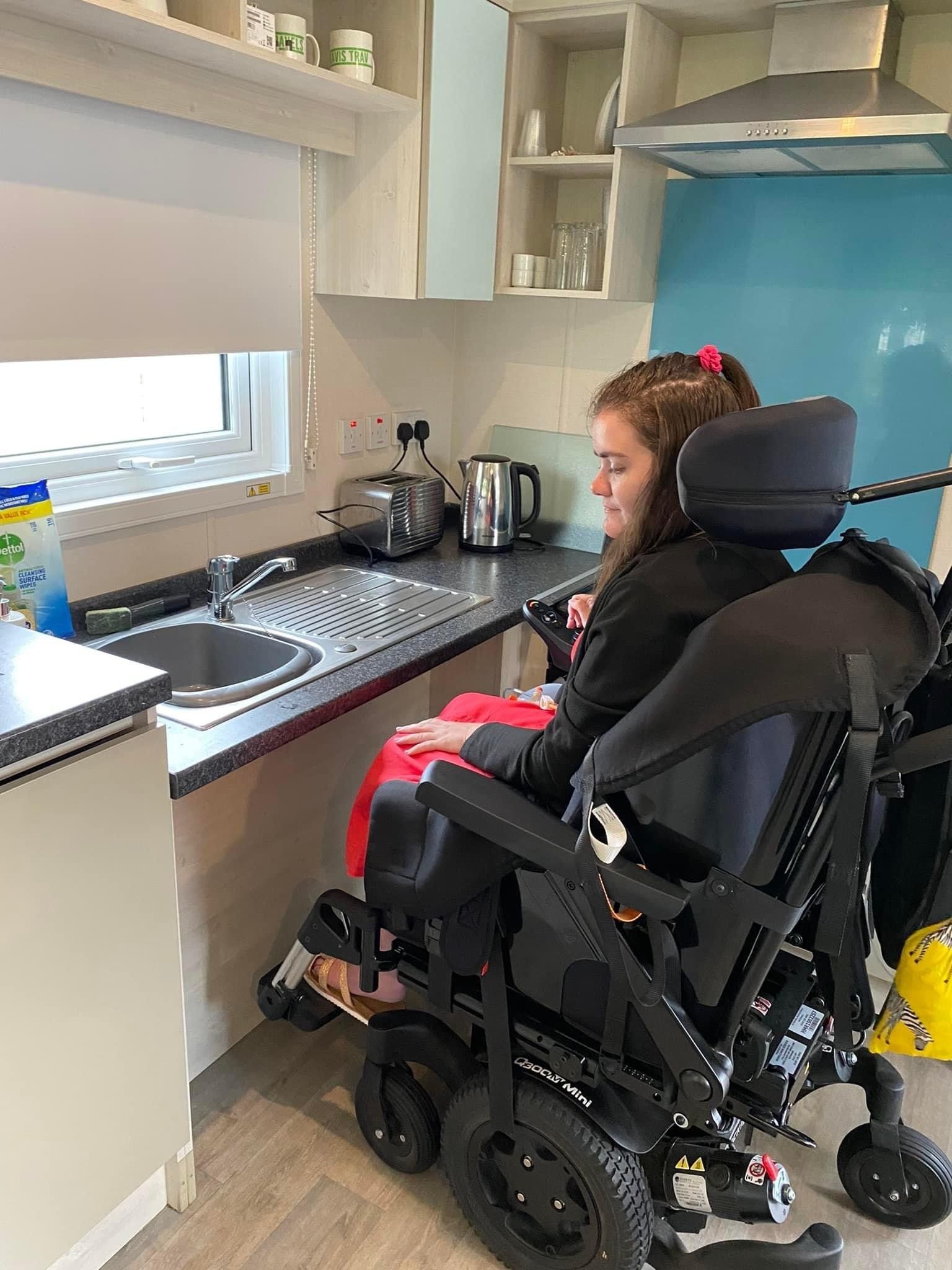 an image of a young lady in her wheelchair showing herself positioned near the kitchen sink and how easy it is to access