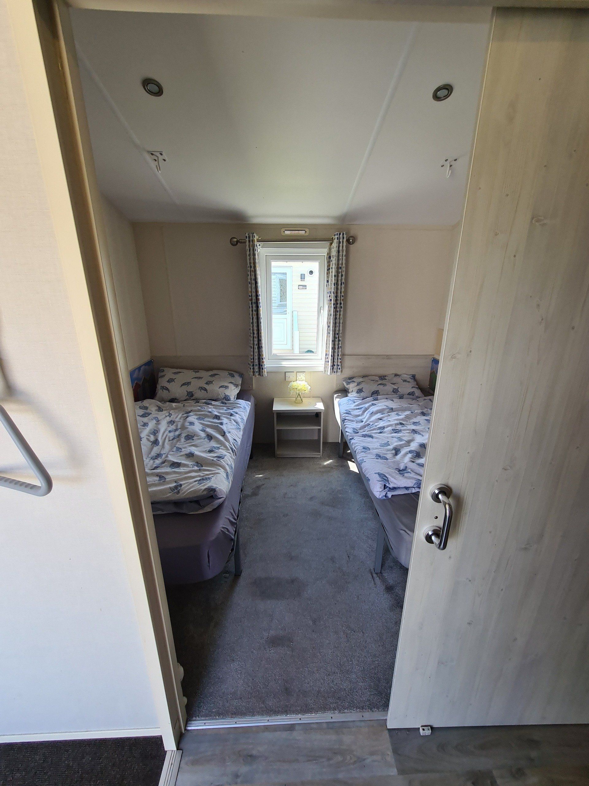 a view inside the second bedroom of the sign along with us foundation caravan showing two single beds seperated by a bed side cabinet with overhead hooks for manual grab handles