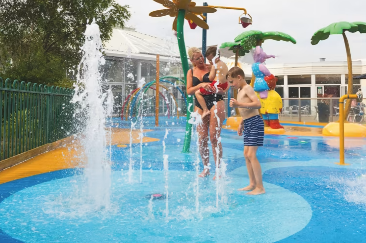 an image of a women and her two children playing in the accessible colourful splash zone on the haven cala gran holiday park