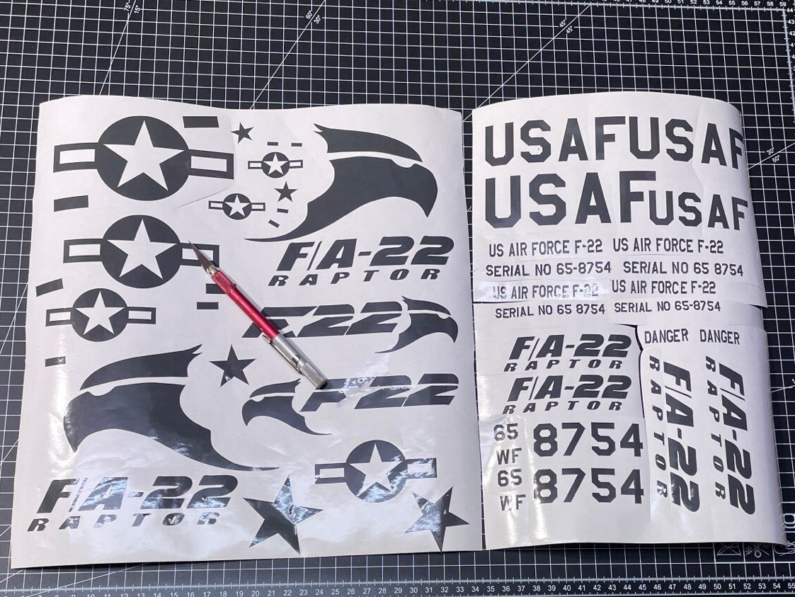 Decals für die F-22. Aufgrund der aufwendigen Lackierung reichte mir hier dunkelgraue Folie. Du siehst hier etwa doppelt soviele Decals, wie ich hinterher tatsächlich genutzt habe. Decals und Aufkleber für die F-22 Raptor aus grauer Folie.