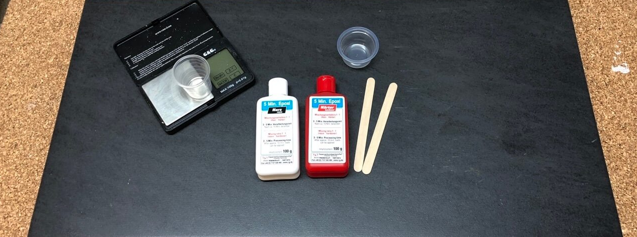 5-Minuten Epoxy mit Zubehoer. Fehlt nur noch Spiritus und Handschuhe. Wichtig ist, grammgenau abzumessen. 5 Minuten Epoxy aufder Arbeitsplatte auf dem Tisch.
