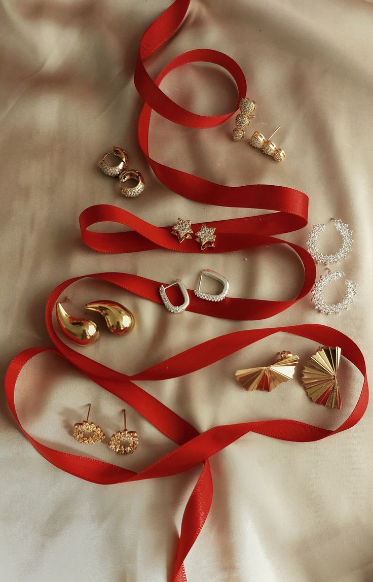 Goldene Ohrringe und Schmuckstecker auf Satinuntergrund – edles Accessoire-Flatlay mit rotem Band.“