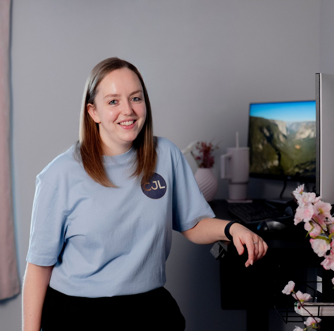 Chrissy wearing blue CJL t-shirt at a standing desk looking at the camera