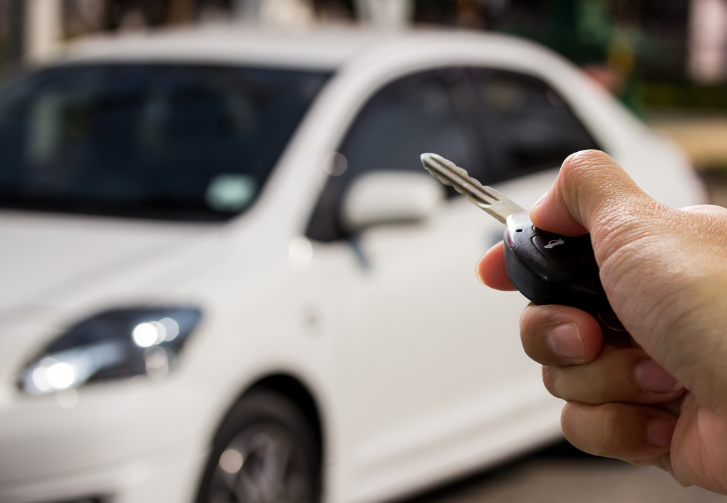 A hand holding a car key pointed at a white car