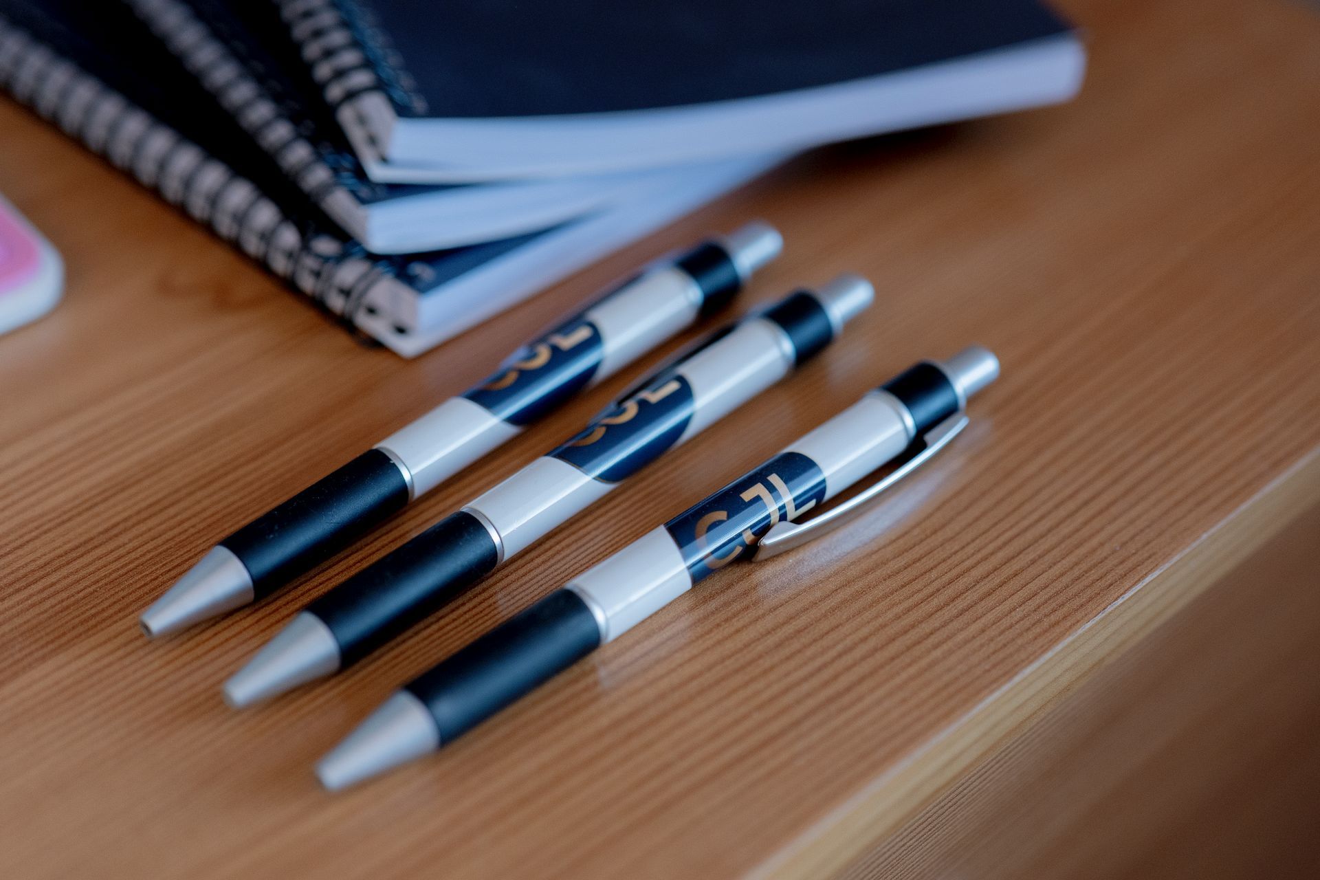 CJL branded pens on a desk with notebooks and a pink calculator