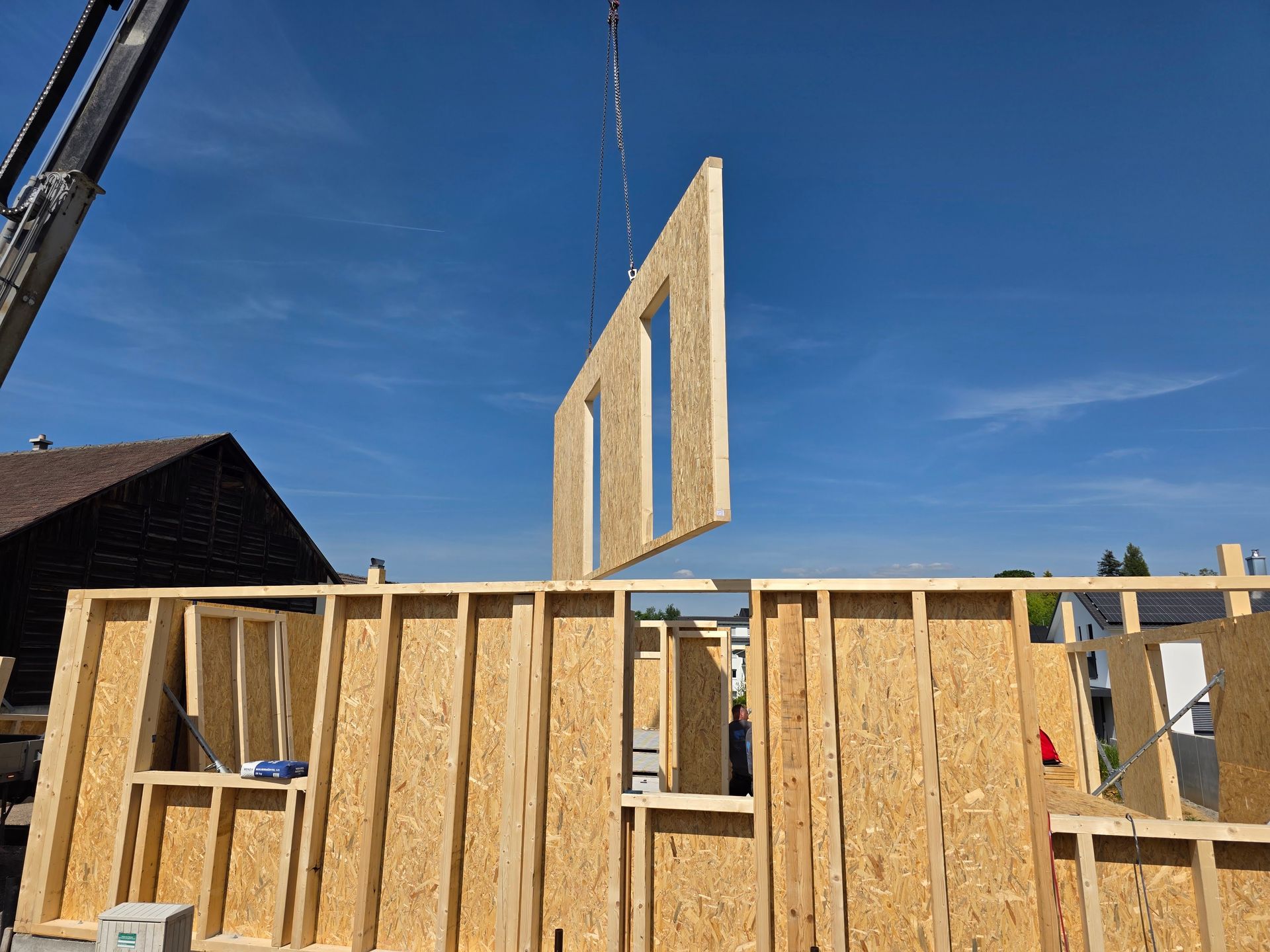 Offene Baustelle mit Kran, der gerade eine Wand anhebt.