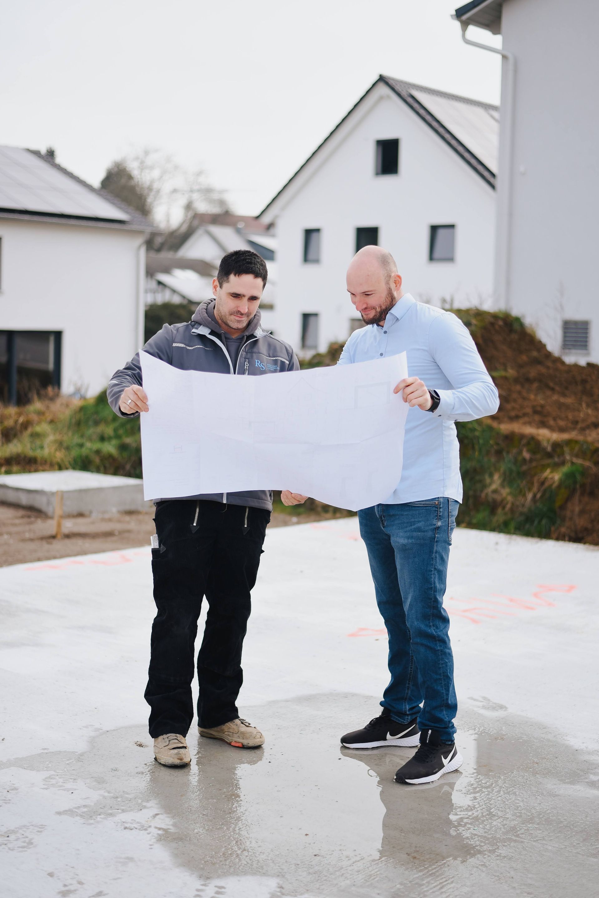 Zwei Männer der RS Bau und Immobilien GmbH stehen auf einer Baustelle und begutachten gemeinsam einen Bauplan.