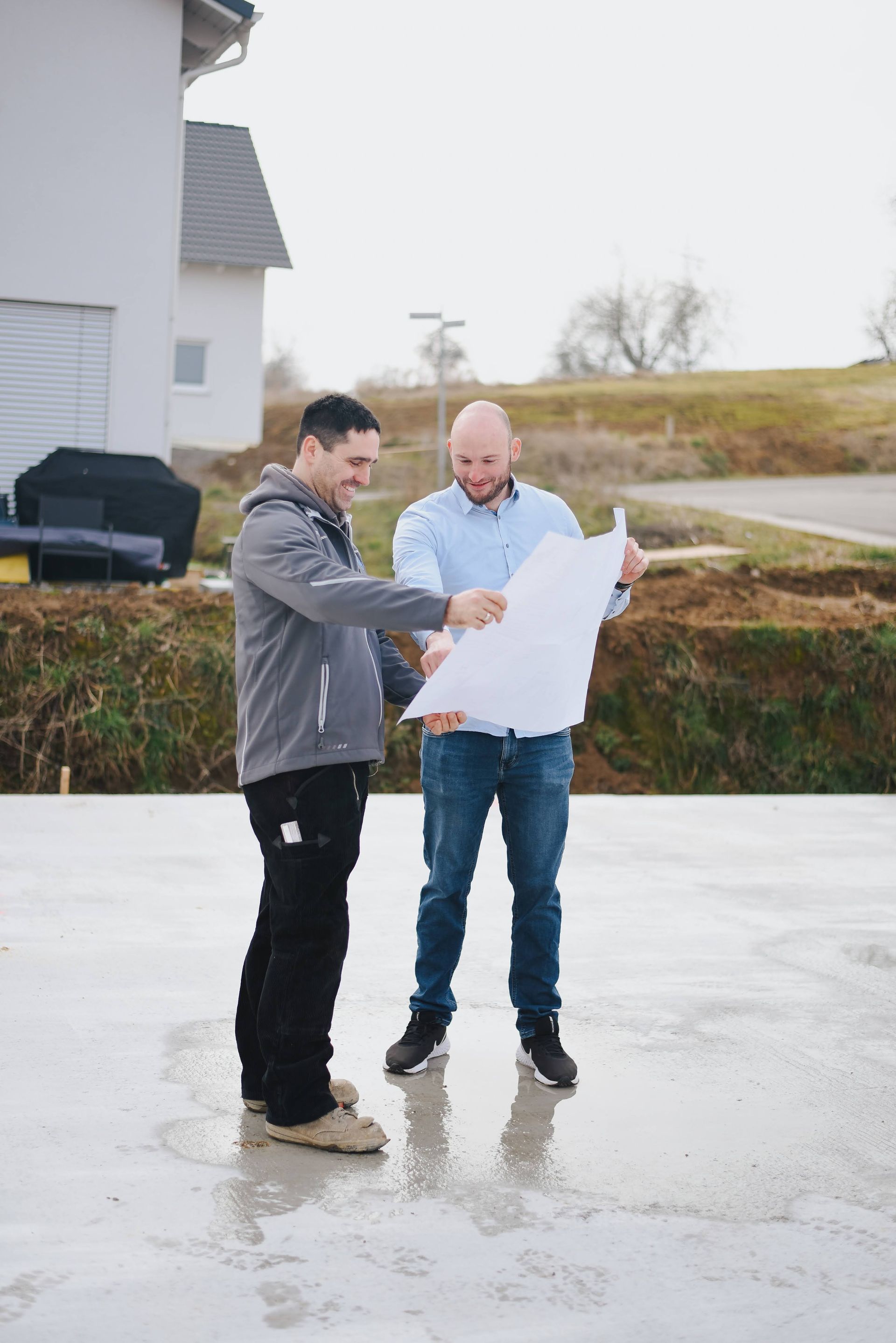 Zwei Männer auf einer Baustelle schauen sich gemeinsam einen Bauplan an.