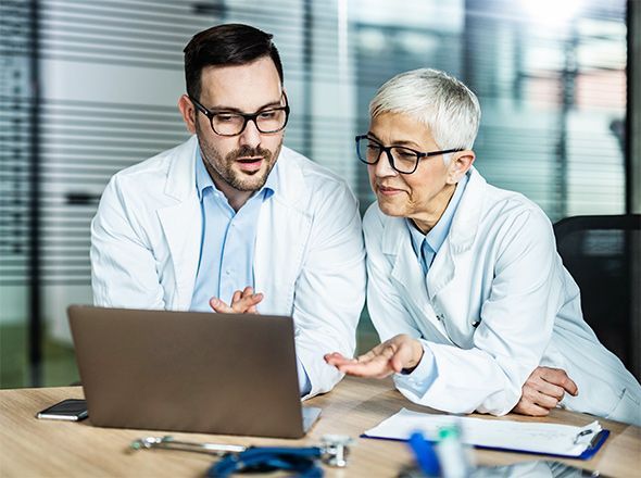 Praxisfinanzierung – junger Arzt und ältere Ärztin schauen auf Laptop